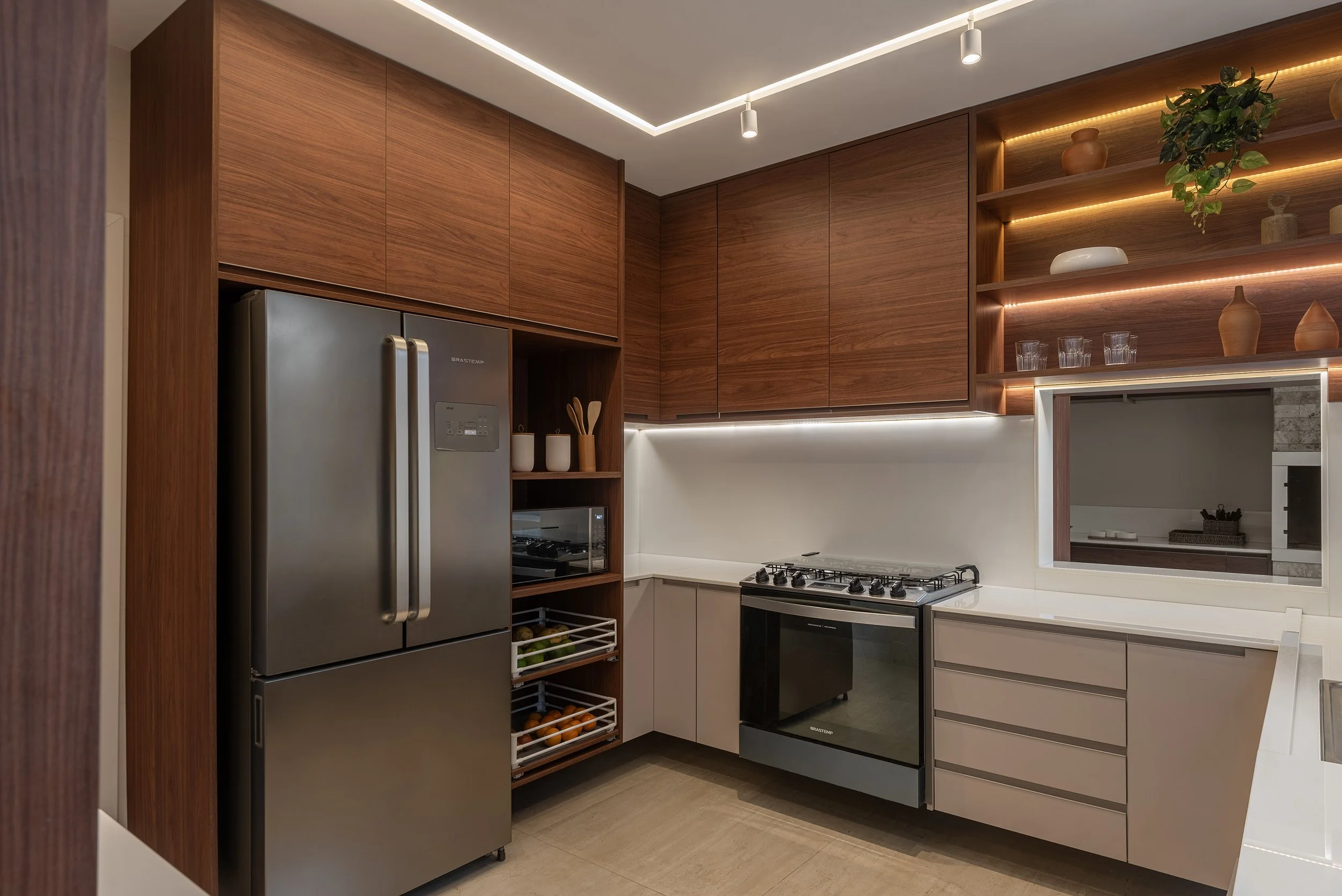 Modern kitchen with wooden upper cabinets, white lower cabinets, stainless steel fridge, gas stove, open shelving with decorative vases and glassware, and a small window with mirror reflection.