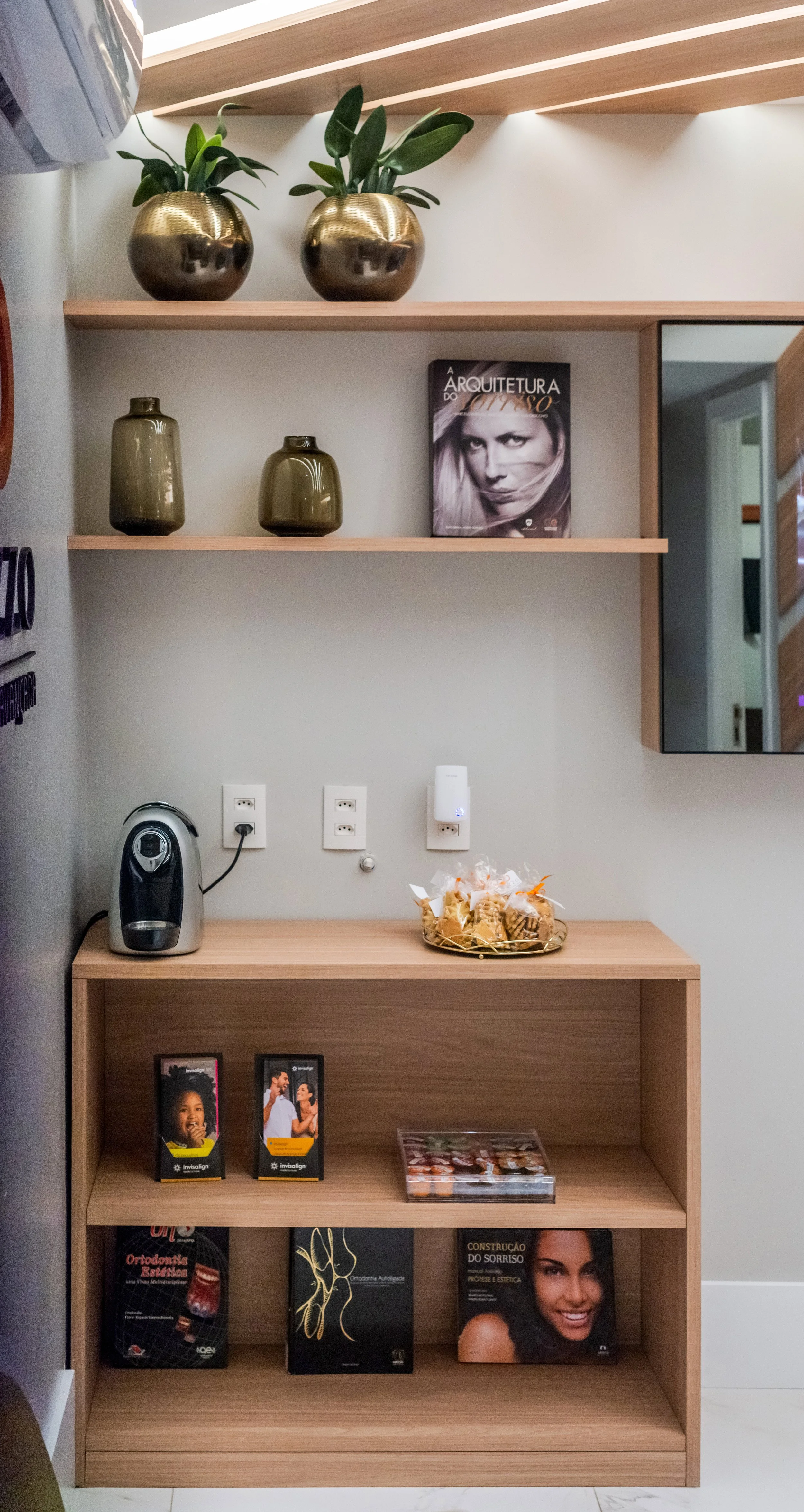 Interior with two green vases and twogold vases with plants on a wooden shelf, a magazine, a small appliance, and a wooden cabinet with brochures and decorative items.