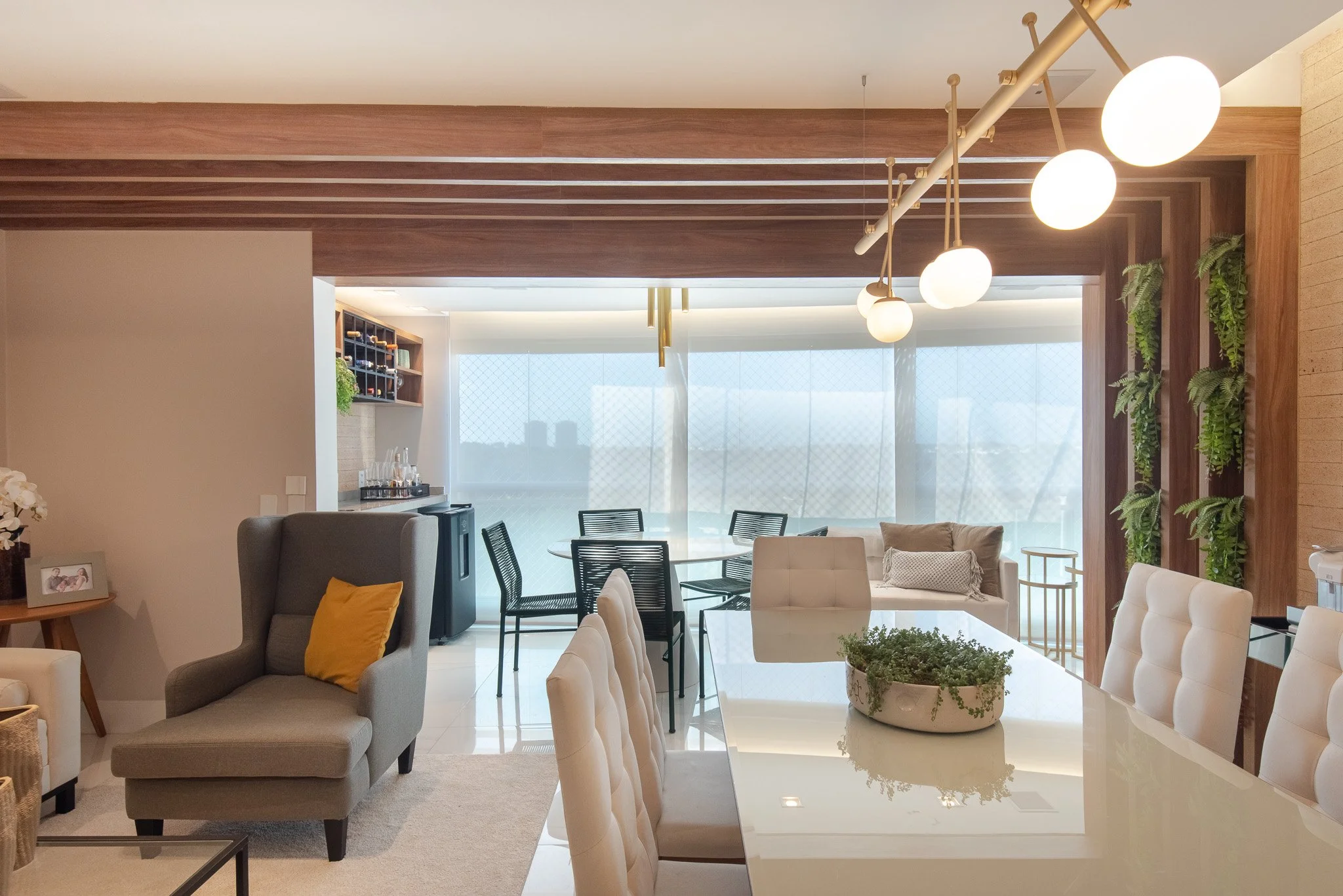 Modern living room with dining area, beige chairs, green plants, and large windows with city view.