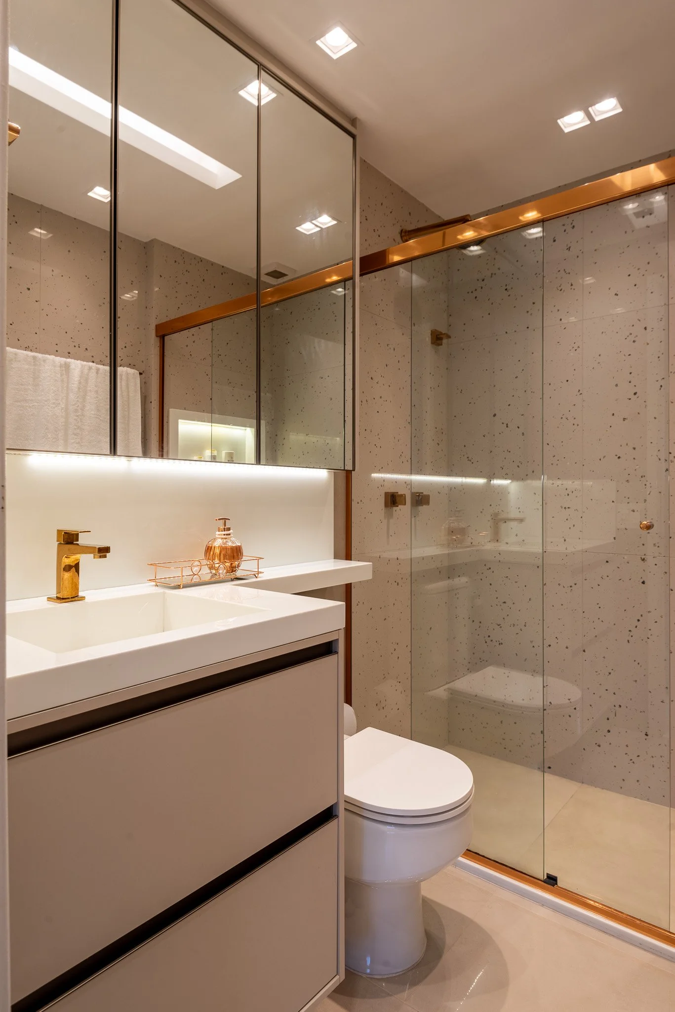 Modern bathroom with a white vanity and gold fixtures, mirrored cabinet above, glass shower enclosure, and neutral tones.