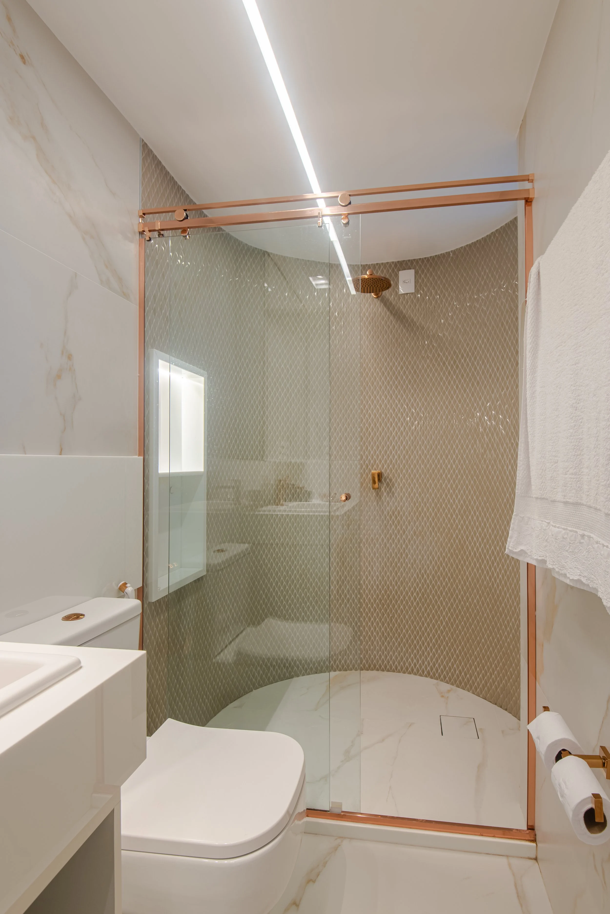Modern bathroom with a walk-in shower enclosed by clear glass, featuring beige diamond-patterned tiles, a rainfall showerhead, marble floor, white toilet, and a white towel hanging on a wall-mounted rack.