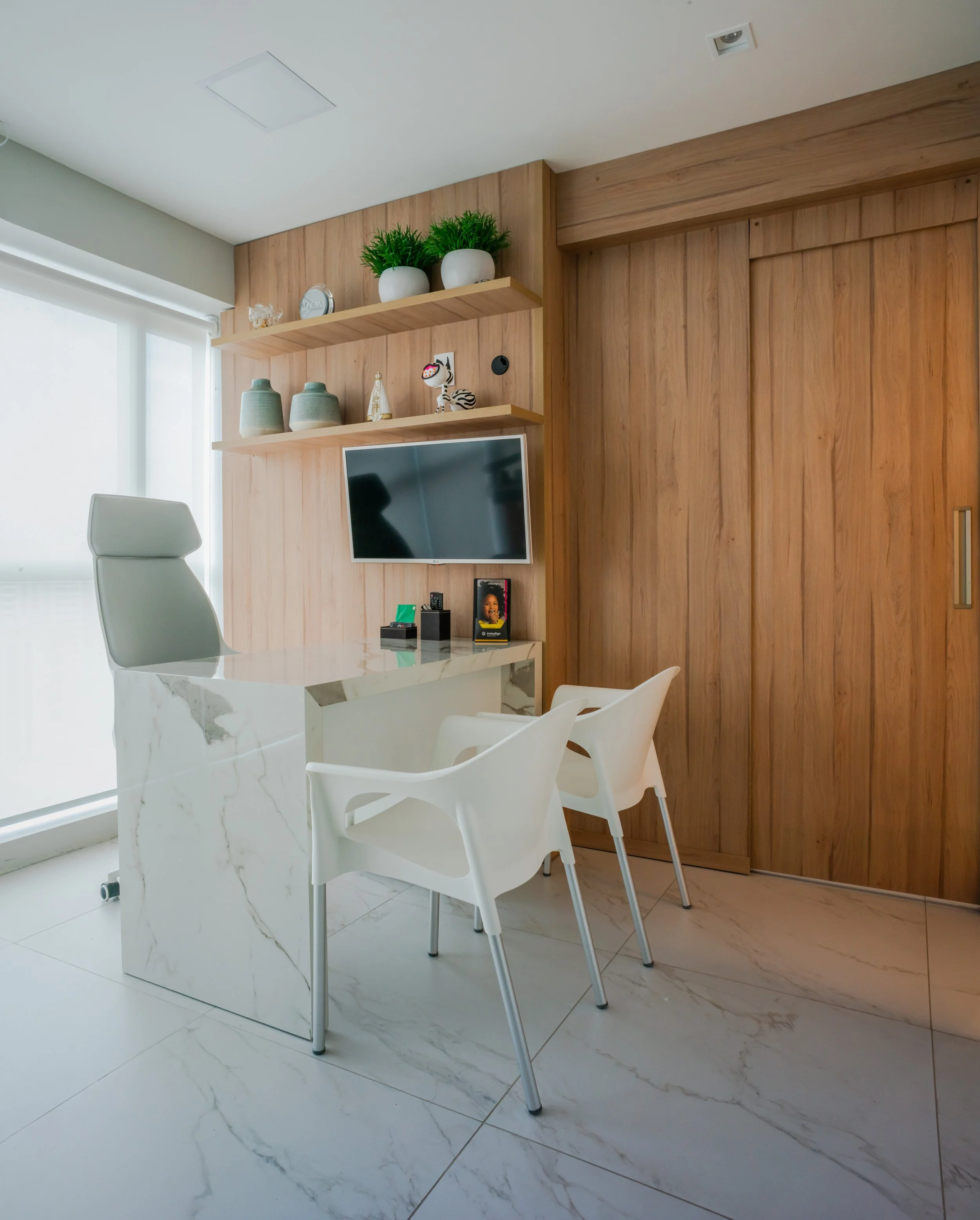 Modern office with marble desk, white chairs, wooden wall panels, and decorative items on shelves.