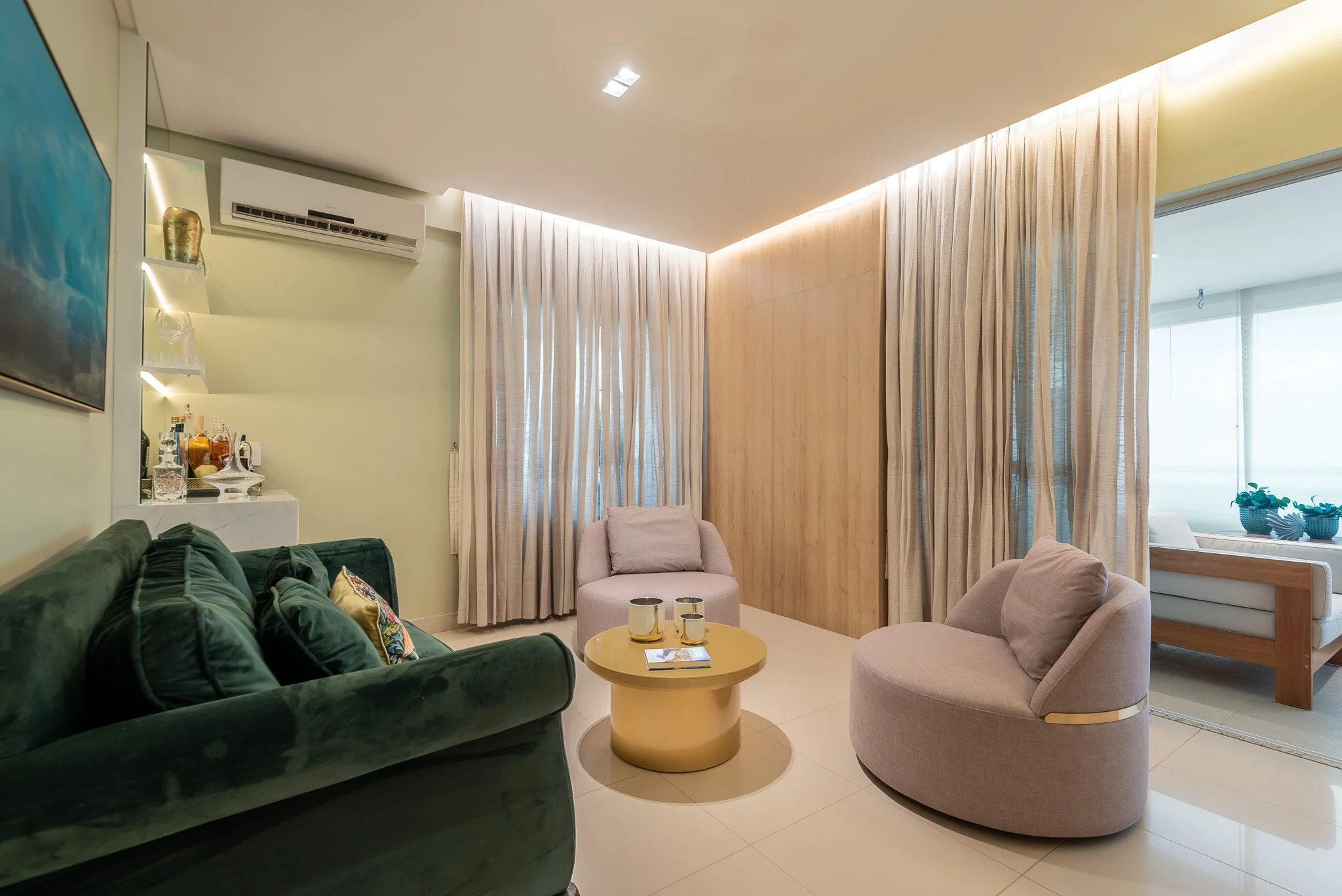 Modern living room with a green velvet sofa, beige armchairs, a round coffee table, curtains, and a view outside through glass doors