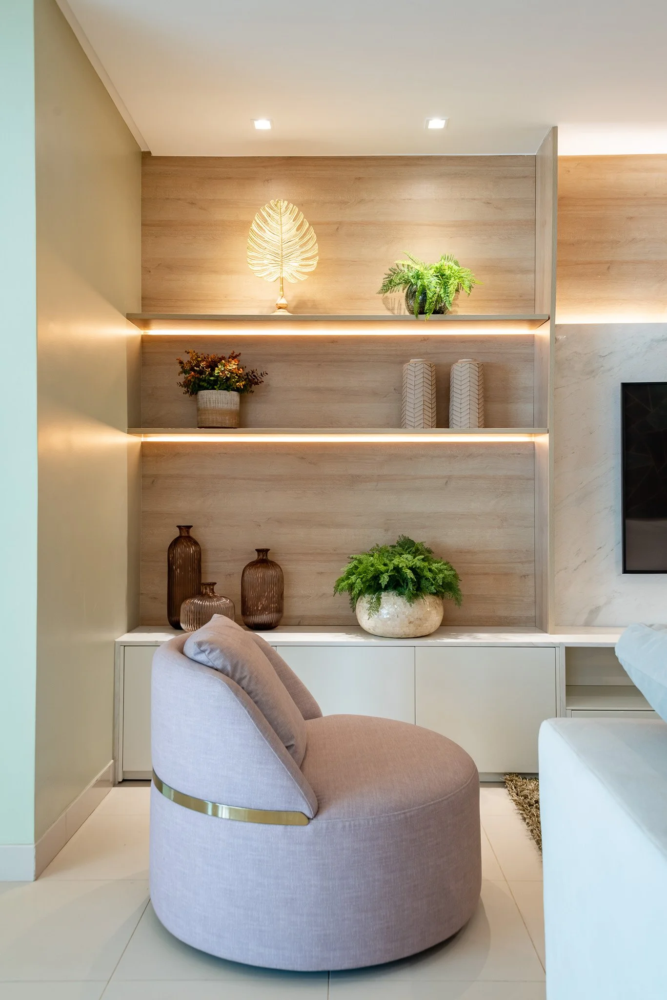 Modern interior living room with built-in wall shelves decorated with plants, vases, and decorative items, beige armchair, and white cabinet.