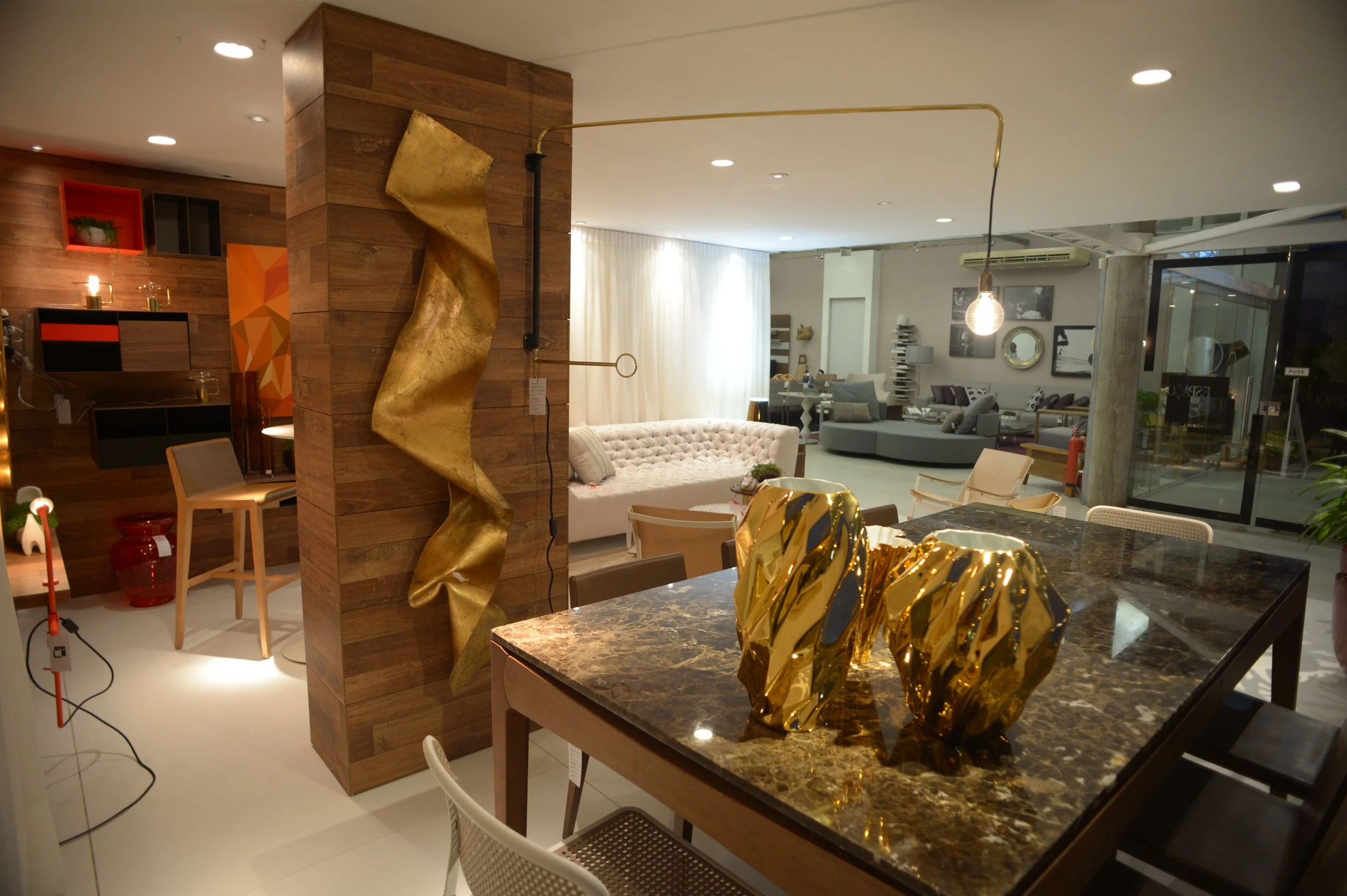 Interior of a modern furniture store with various sofas, a marble dining table, and decorative metallic sculptures.