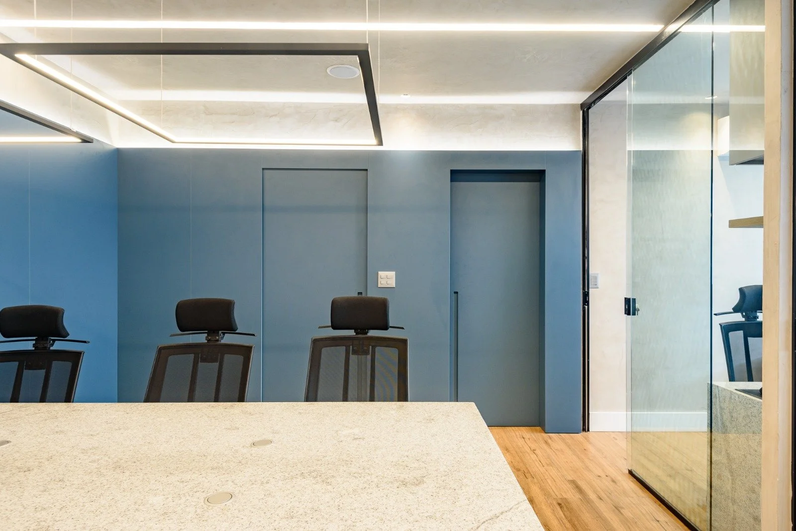 Modern conference room with blue walls, glass partitions, and black office chairs
