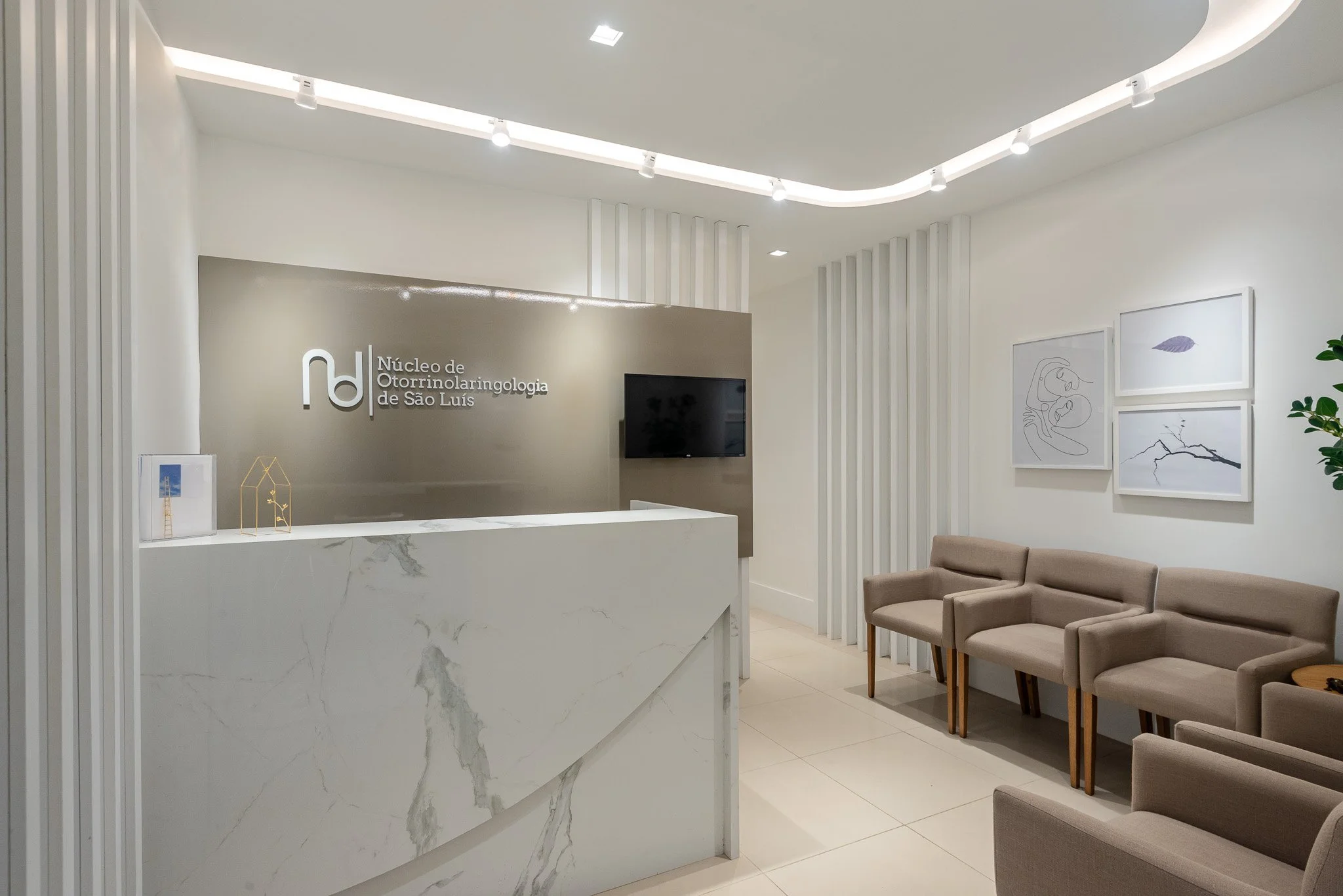 Modern waiting room with white walls, beige chairs, a white marble reception desk, and framed wall art.