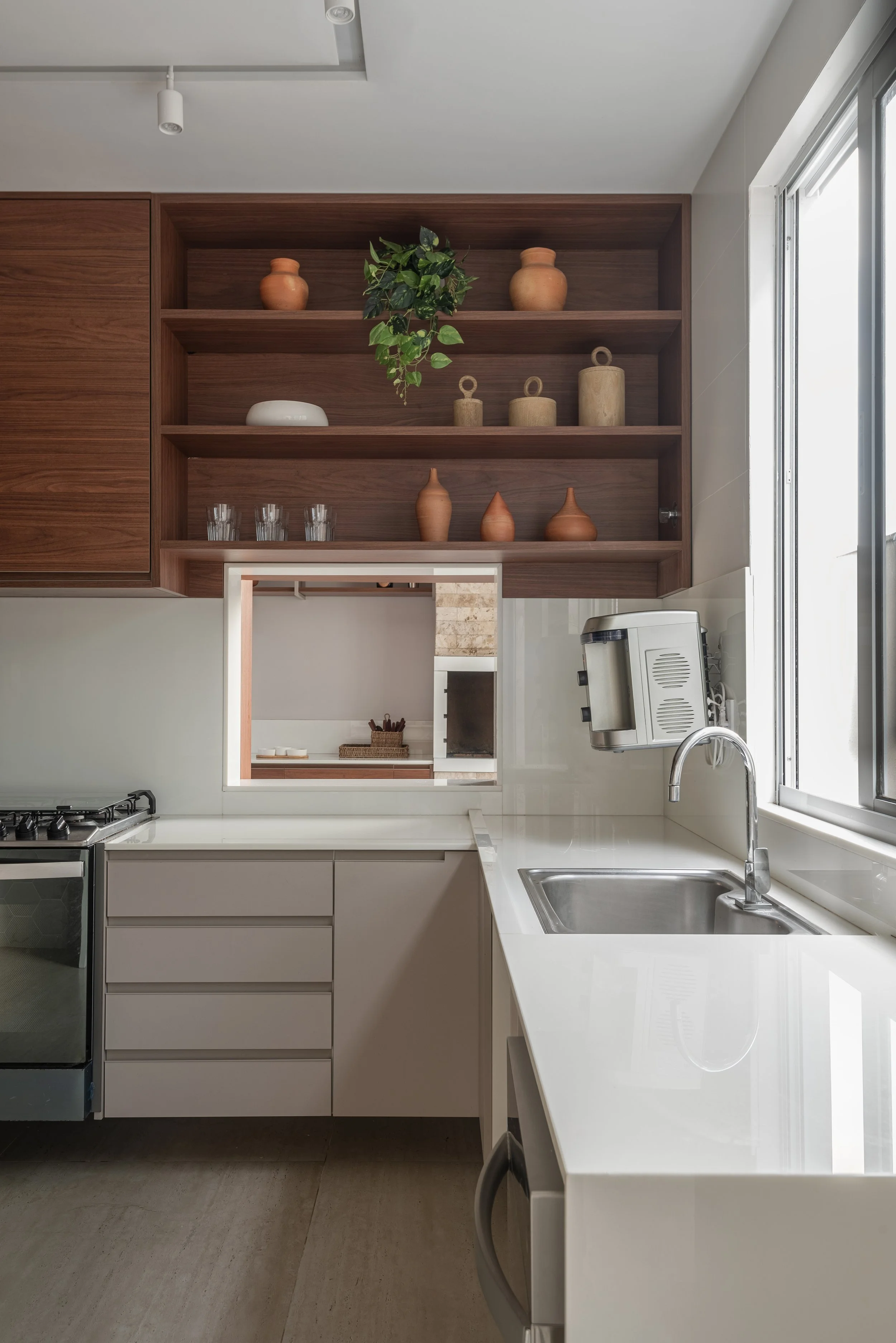 Modern kitchen with white countertops, a stainless steel sink, and wooden open shelves displaying potted plants, vases, and glass containers.