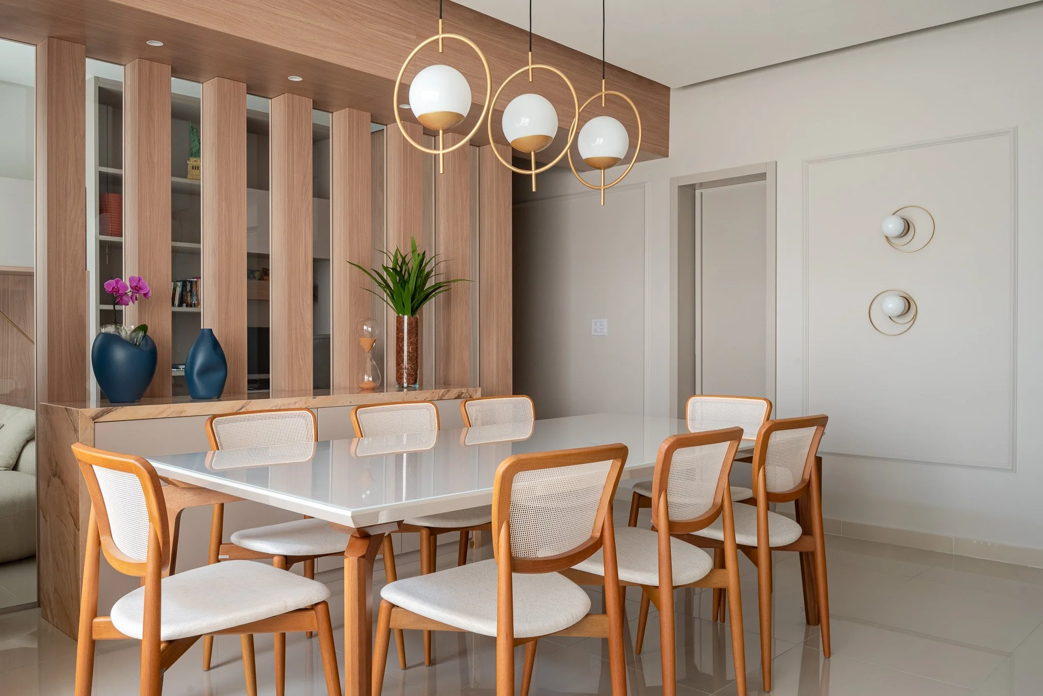 Modern dining room with wooden chairs, a glass table, and decorative vases on a console, with a wooden partition and pendant lights.