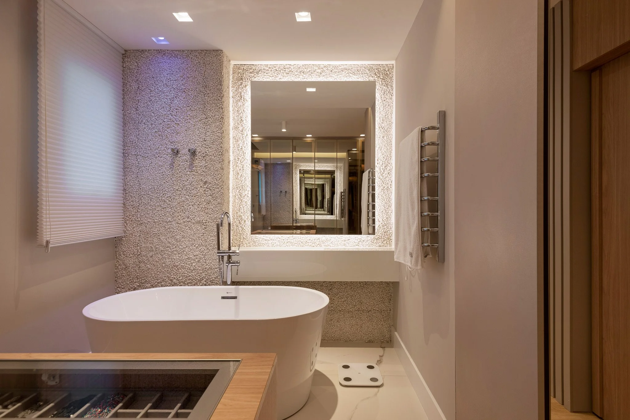 Modern bathroom with a standalone bathtub, large mirror, towel rack, and textured wall.