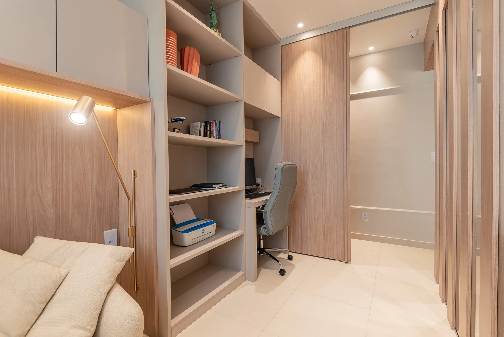 A cozy bedroom corner with a bed, built-in shelving, a desk with a computer, and a rolling office chair.