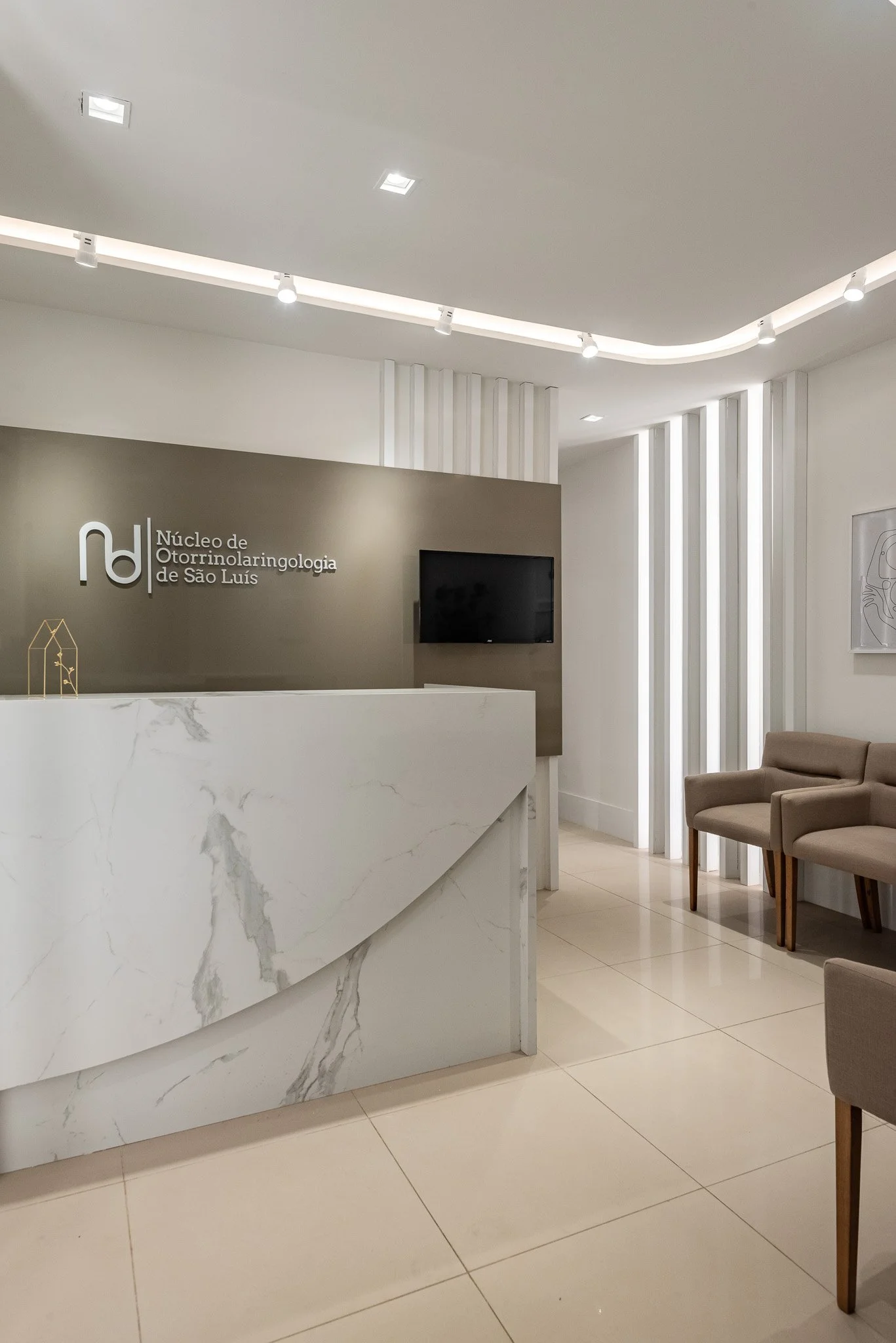 Modern reception area with a marble desk, beige chairs, and a wall with Portuguese text and logo for Núcleo de Otorrinolaringologia de São Luis.