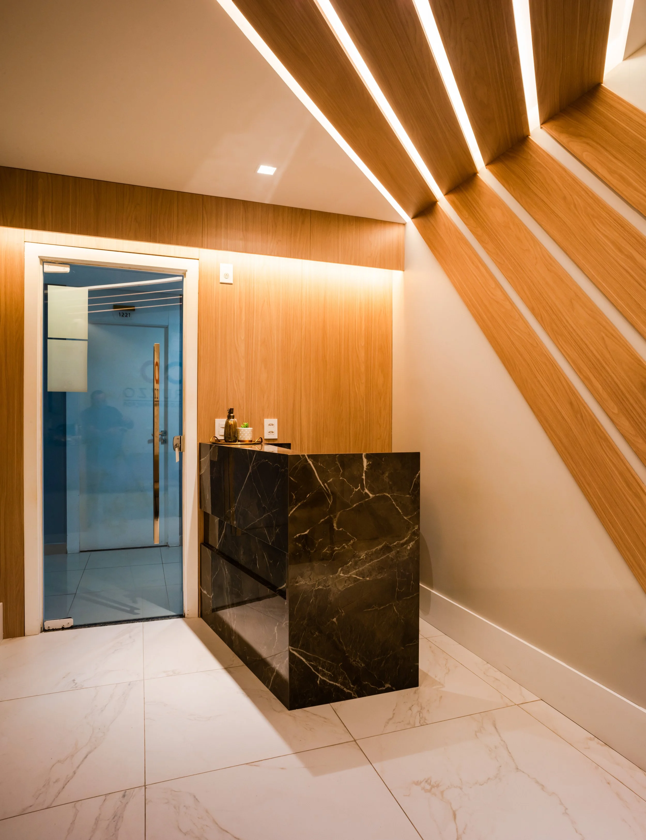 Modern interior space featuring a marble reception desk, wooden wall panels, and a glass door, with a sloped wooden ceiling design.
