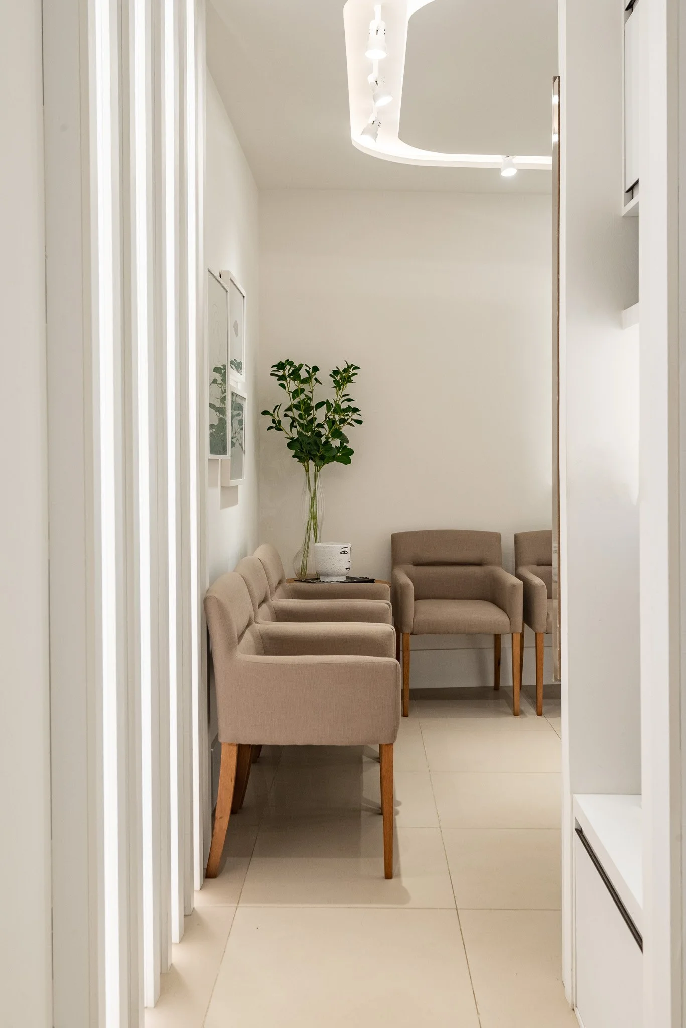 Neutral-colored waiting area with four beige chairs, a green plant, and white wall art, seen through a doorway.