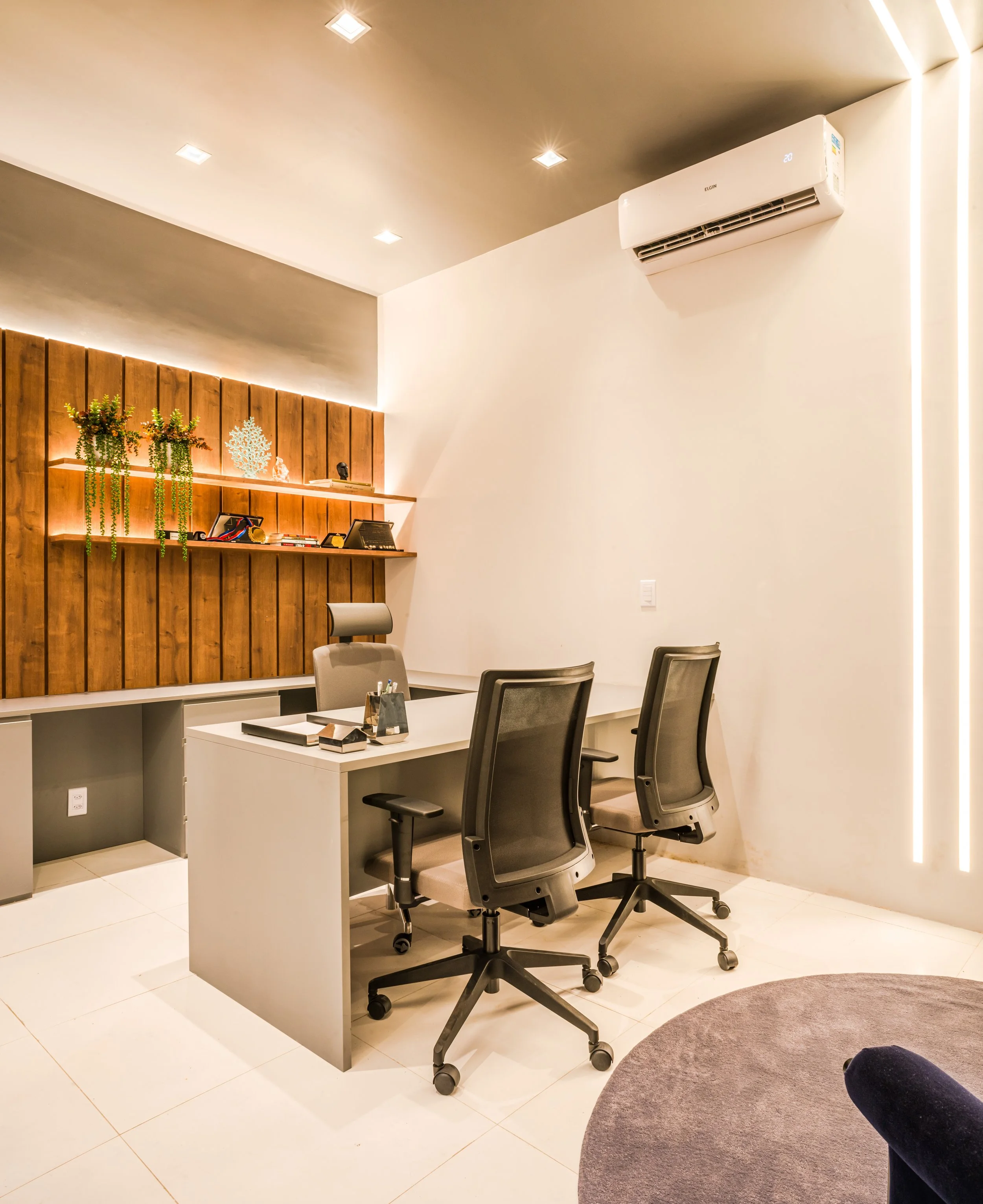 Modern office with white desk, three ergonomic office chairs, wooden wall with shelves and decorative plants, and wall-mounted air conditioner.