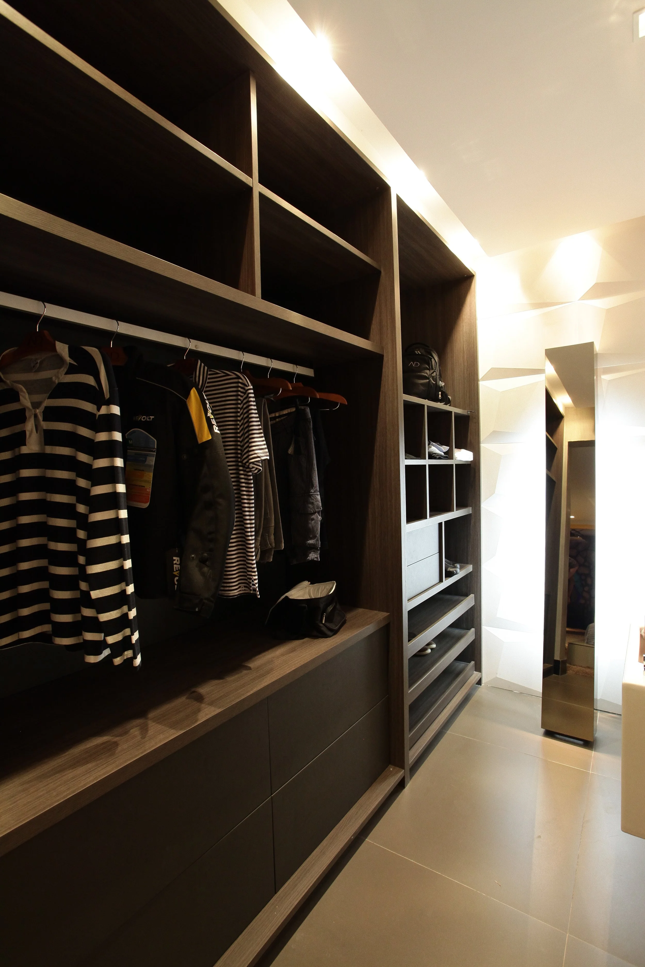 Modern walk-in closet with dark wood cabinetry, hanging clothes, shelves, and a standing mirror.