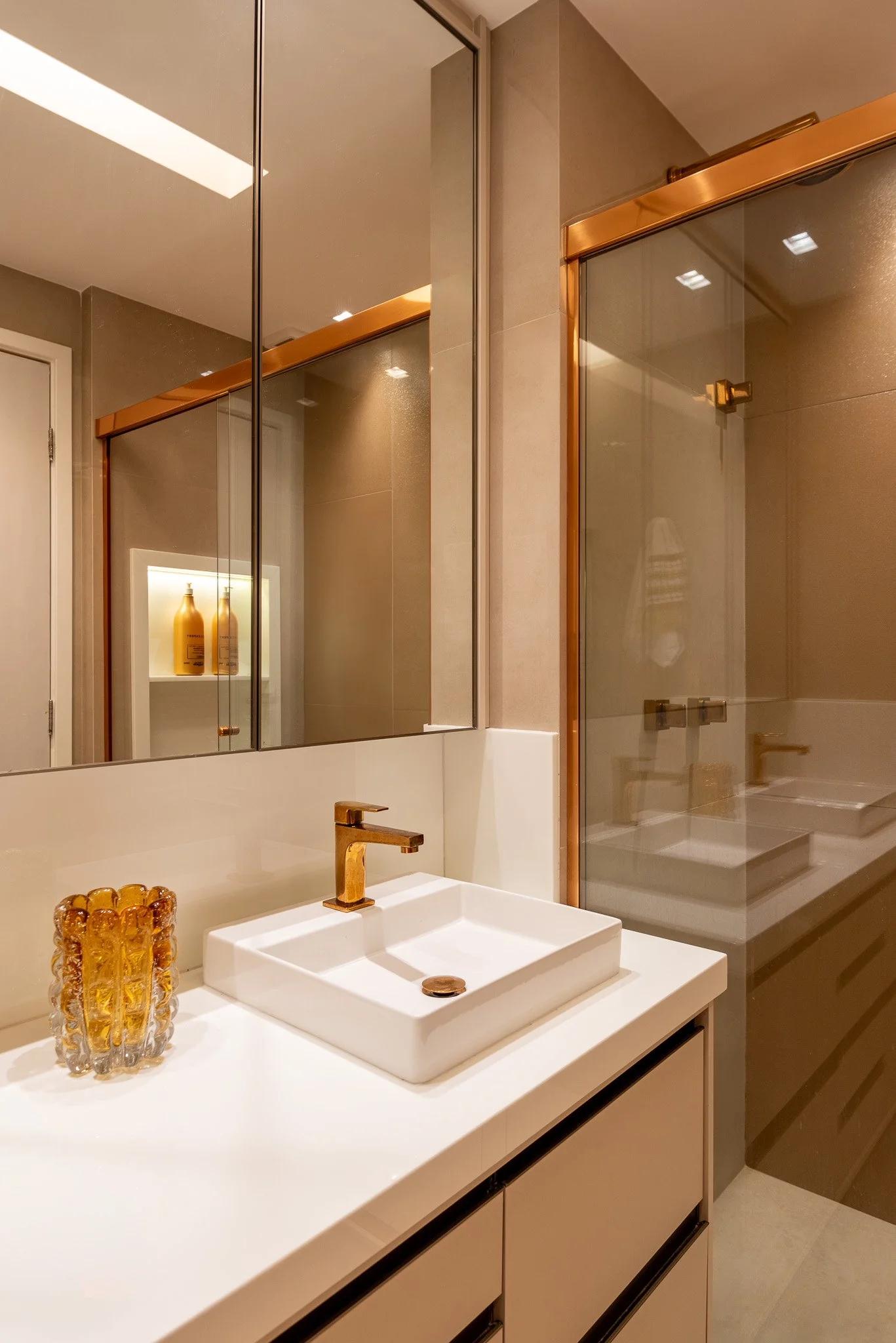 Modern bathroom with a white countertop, square sink, gold faucet, large mirror, and a glass-enclosed shower with gold hardware.