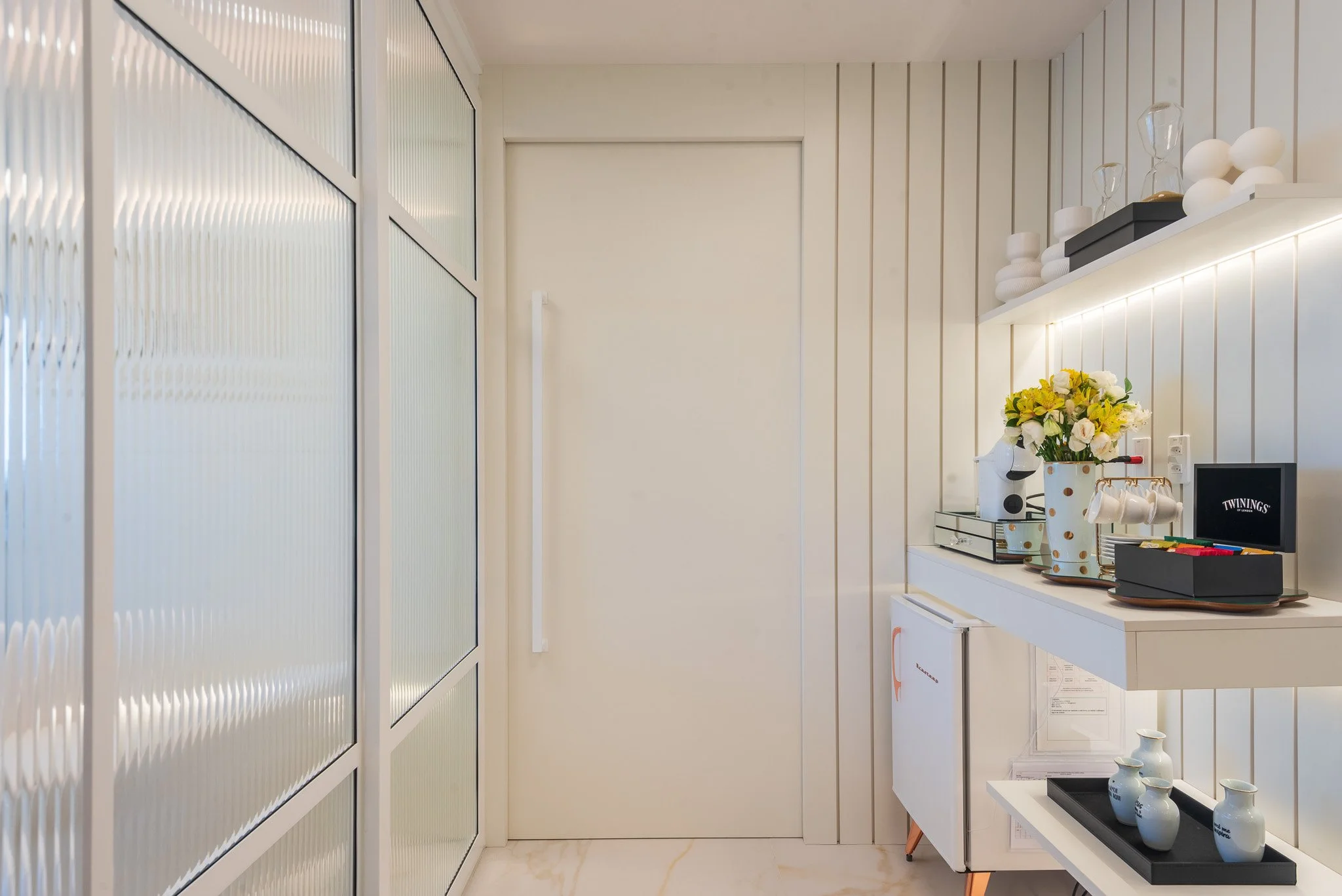 Modern interior space with white paneled walls, decorative vases, flowers, and small appliances on a floating shelf.