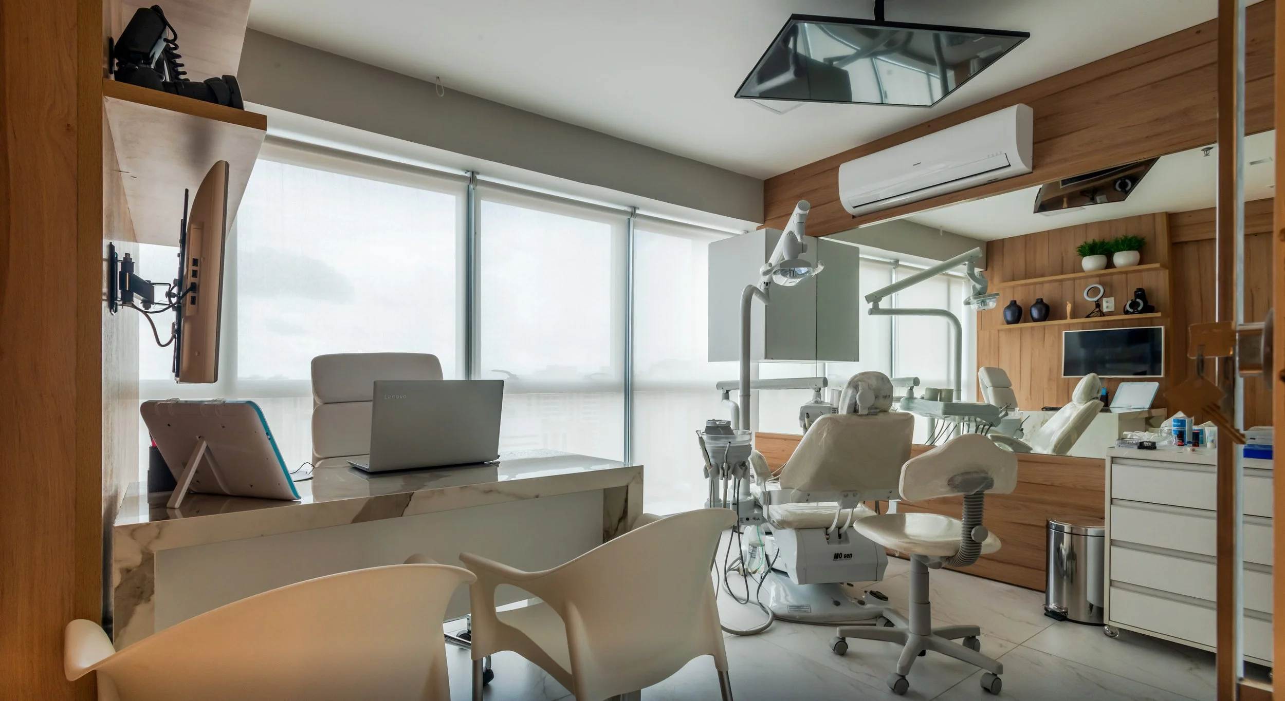 Modern dental clinic with dental chairs, overhead lights, and medical equipment in a brightly lit room with large windows and wooden accents.