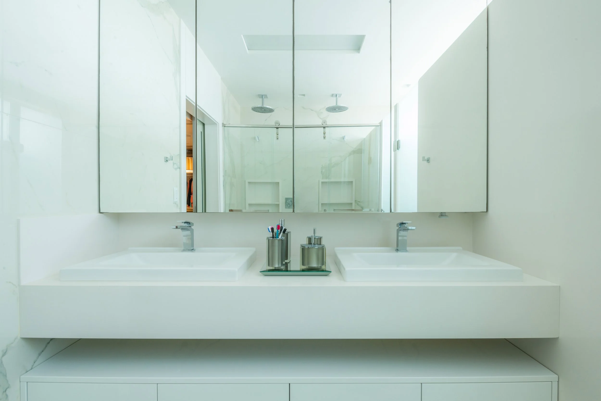 Modern bathroom with double vanity, two white vessel sinks, two silver faucets, a mirror, and bathroom accessories on a tray.