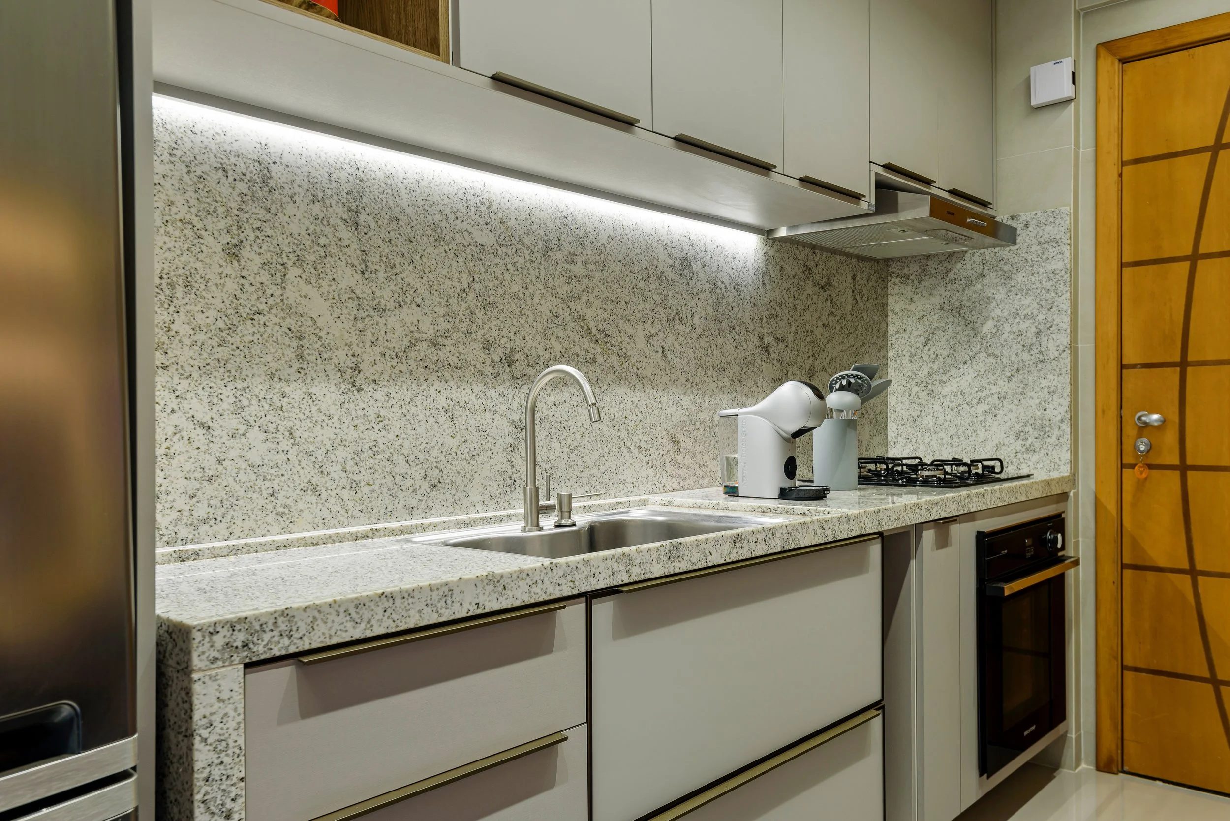 Modern kitchen with speckled granite countertop, sink, coffee machine, gas stove, and wooden door.