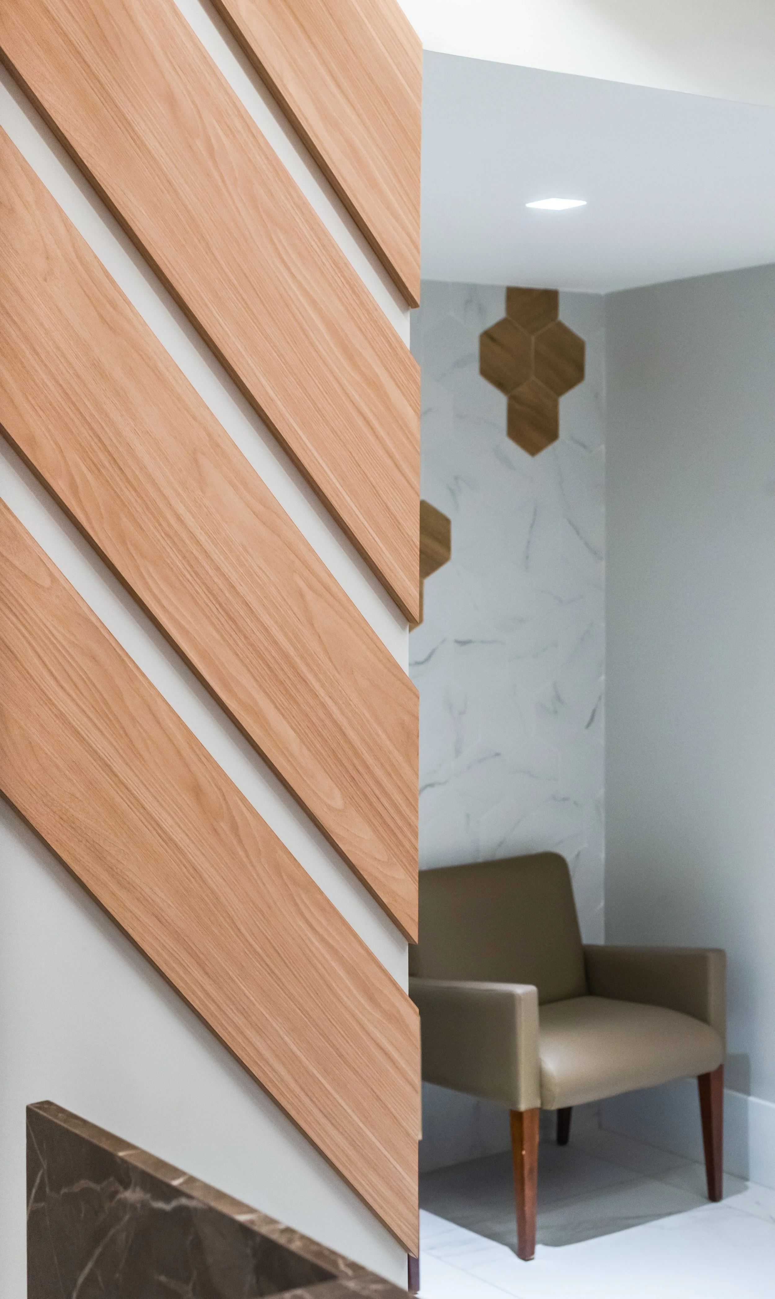 The image shows part of a modern interior with a wooden slat wall design, a beige armchair, and decorative wooden hexagon wall art on a marble-patterned wall.
