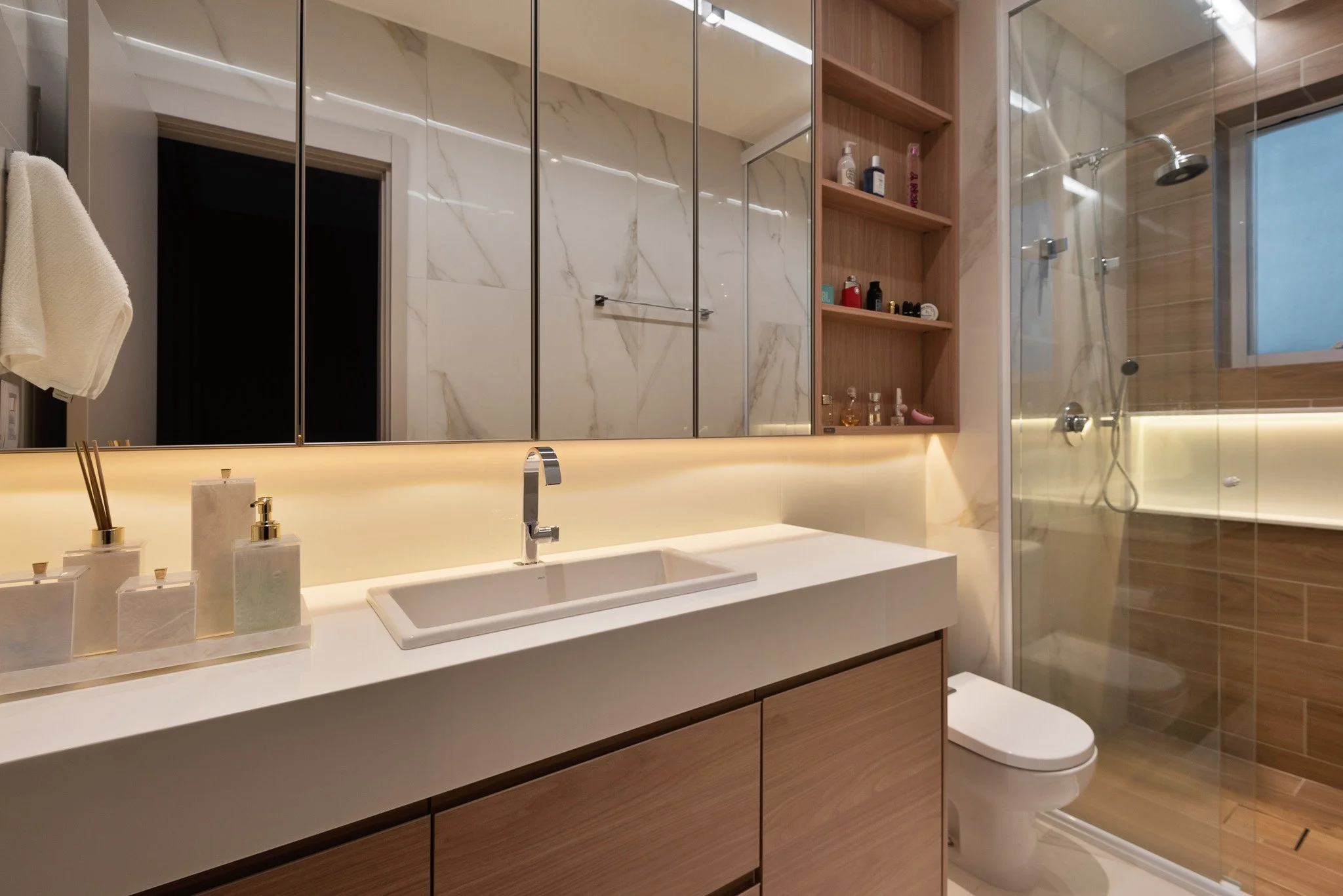 Modern bathroom with a large mirror, white sink, wooden cabinets, and a glass-enclosed shower area with a window.
