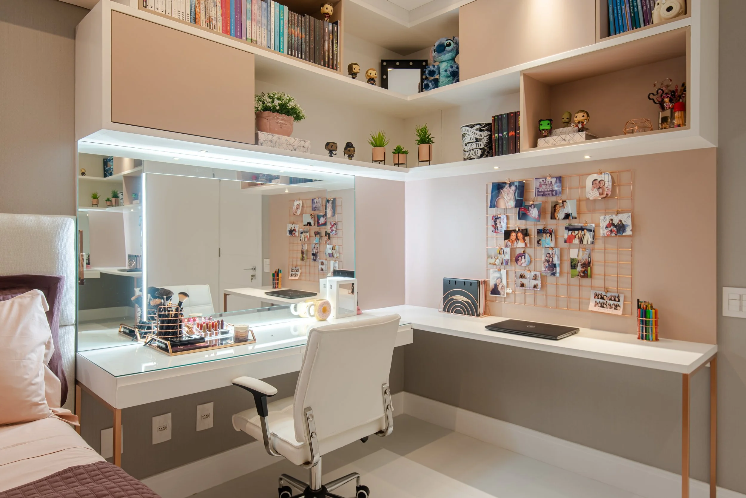 A neatly organized home workspace with white shelves, a large mirror, and a white office chair. The desk holds makeup items, a laptop, and stationery. Decor includes small plants, framed photos, and colorful storage boxes.