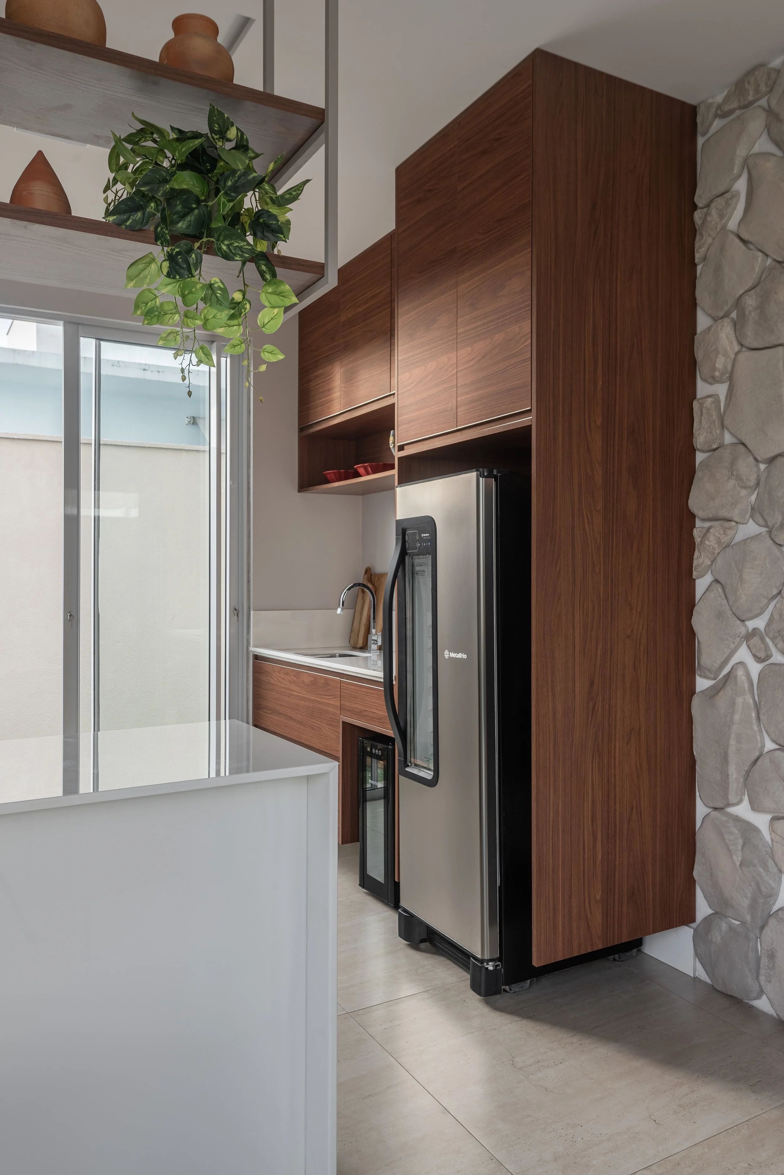 Modern kitchen with wooden cabinets, a stainless steel refrigerator, a stone accent wall, and a sliding glass door with a small outdoor area visible.