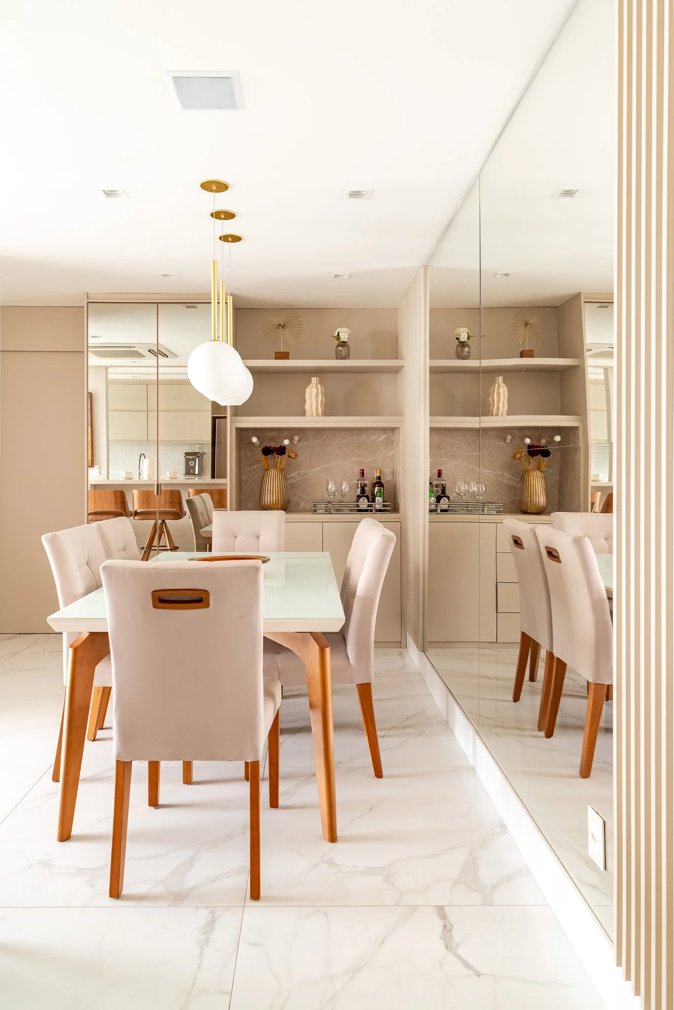 Elegant dining room with a white table, six upholstered chairs, a large mirror, modern pendant lights, and decorative vases on shelves.