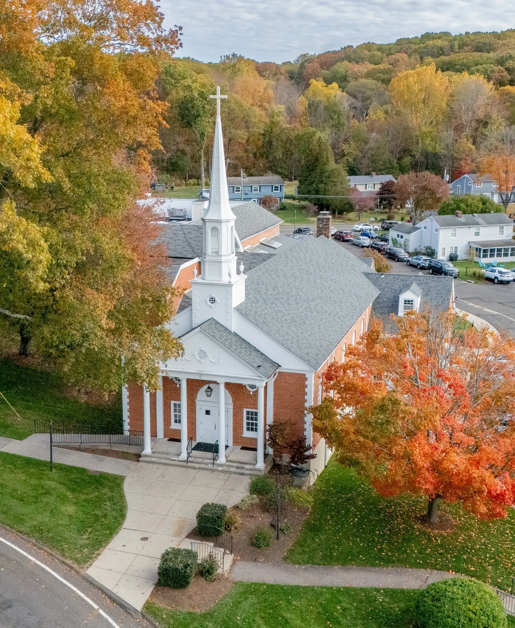 A church building with a steeple surrounded by colorful autumn trees in a small town.