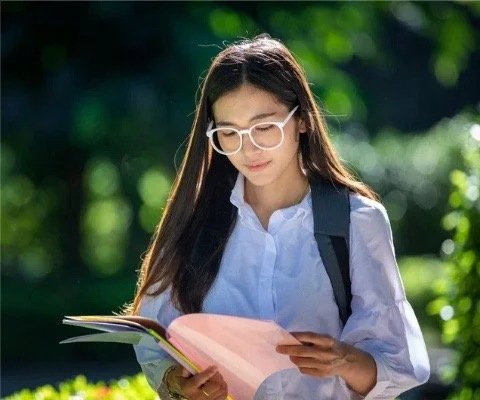 Young woman with glasses reading a book outdoors.