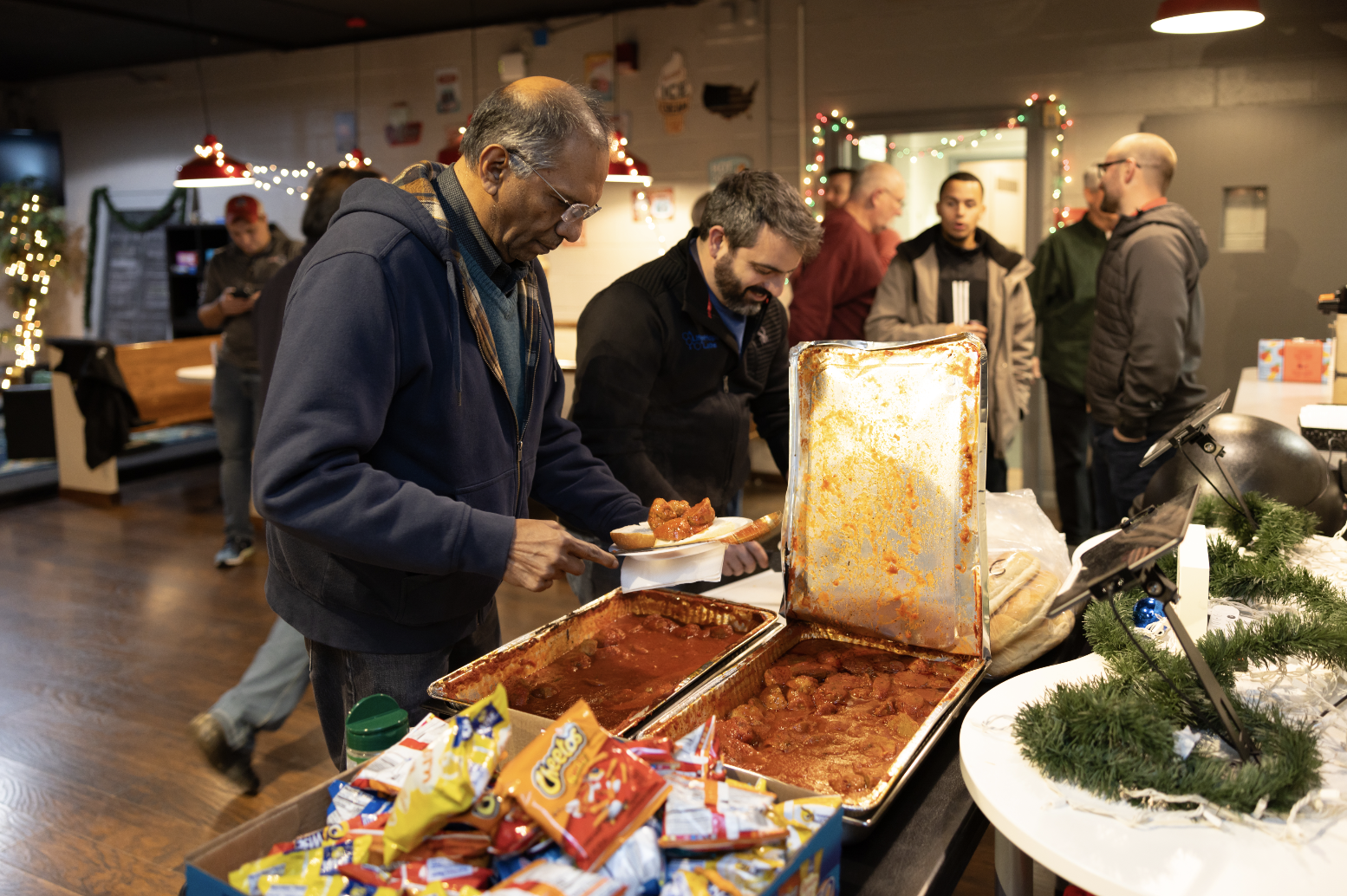 People serving and eating food at a holiday buffet, with festive Christmas decorations in the background.