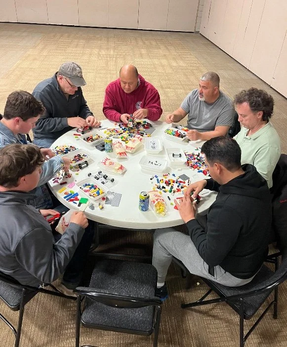 People sitting around a round table assembling LEGO bricks and kits.
