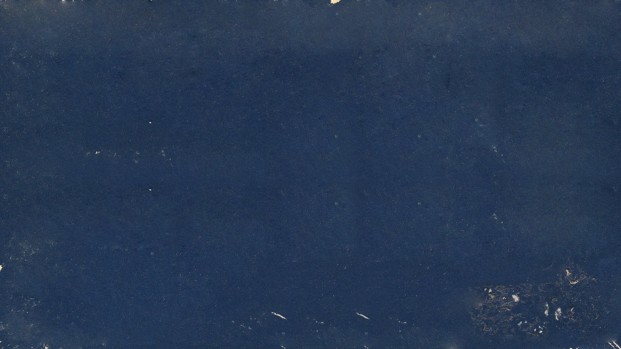 Close-up view of a dark blue surface with small white spots and marks, possibly a textured material or fabric.