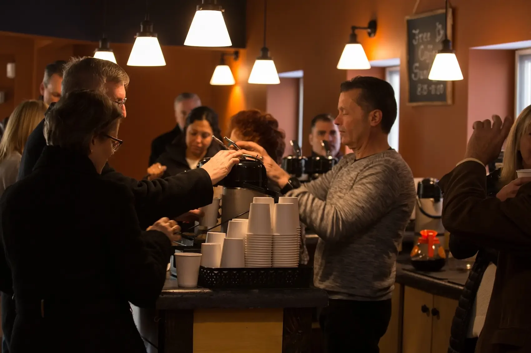 People standing at a coffee bar, ordering drinks, in a cozy cafe with warm lighting and wooden decor.