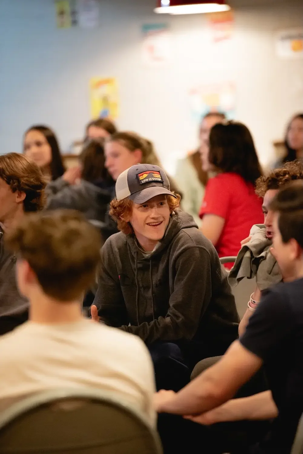 A group of teenagers sitting in a circle, engaging in conversation, in a classroom or community space.