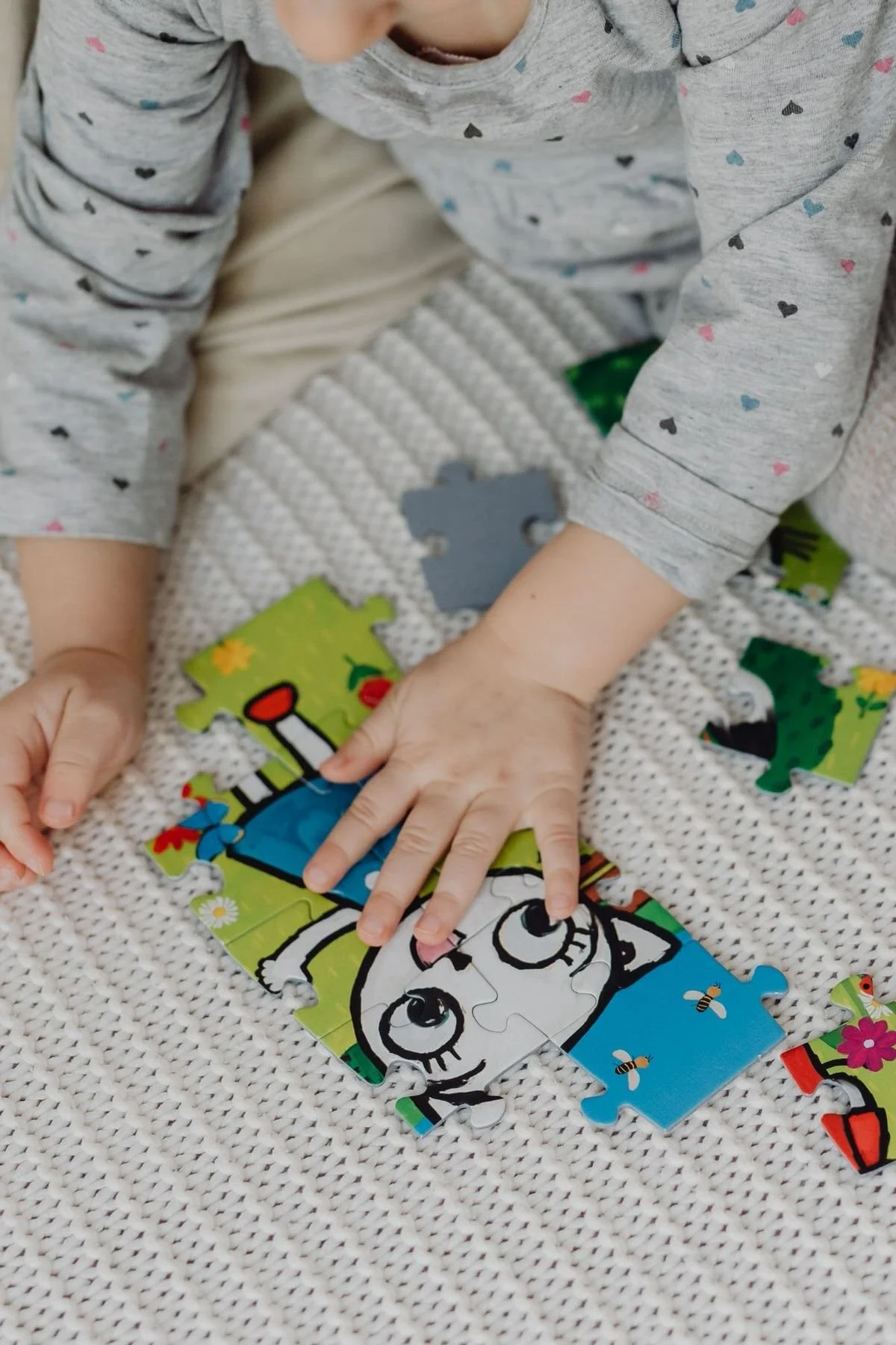 Child assembling a colorful jigsaw puzzle with a cartoon dog on a textured white blanket.