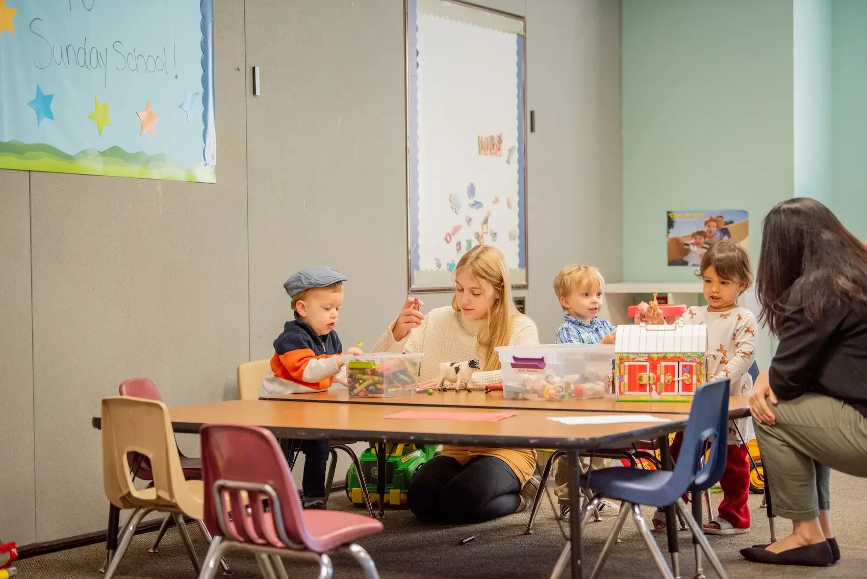 Children and an adult engaged in a craft activity at a table in a classroom.