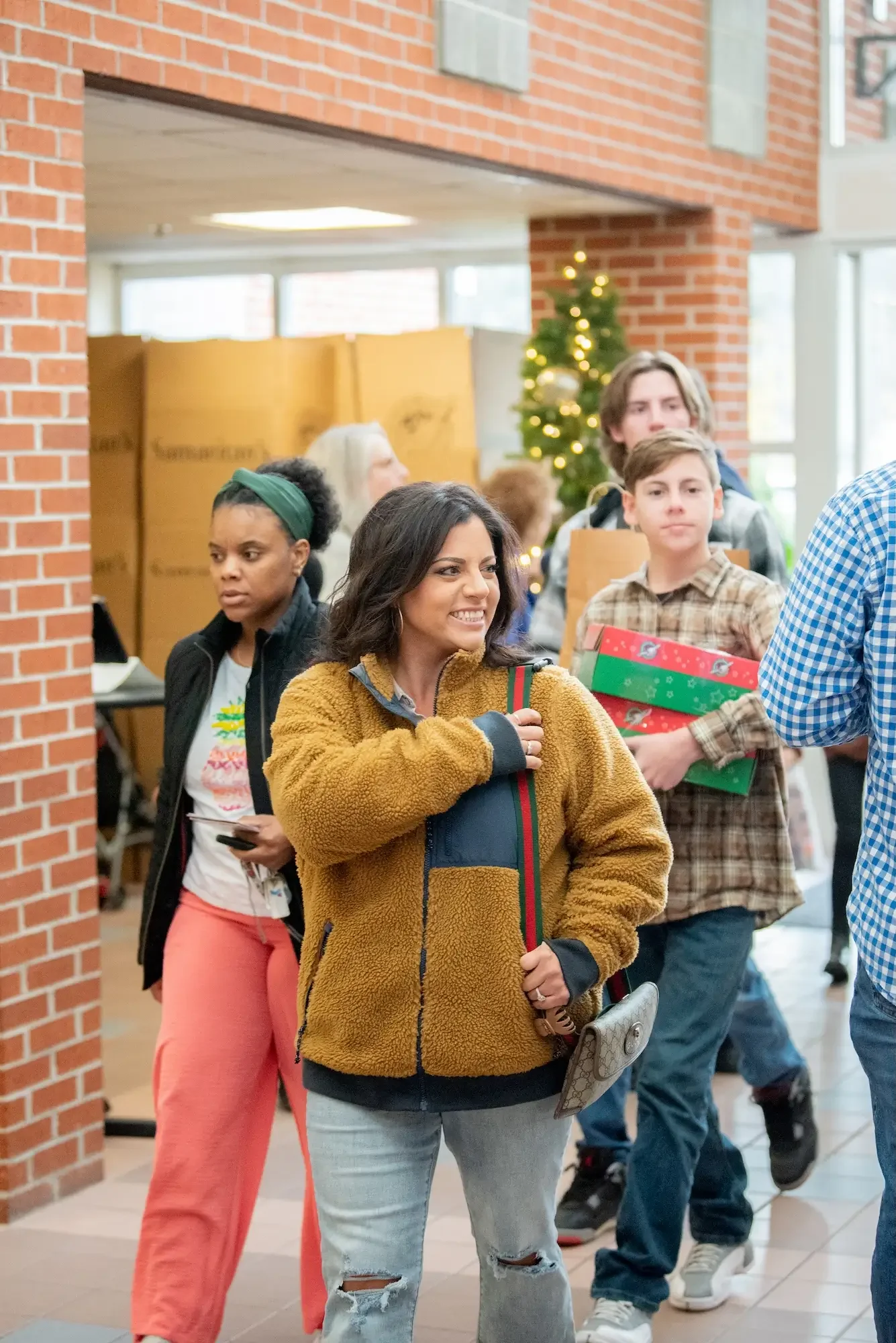 People in a building lobby, some carrying presents, a Christmas tree in the background