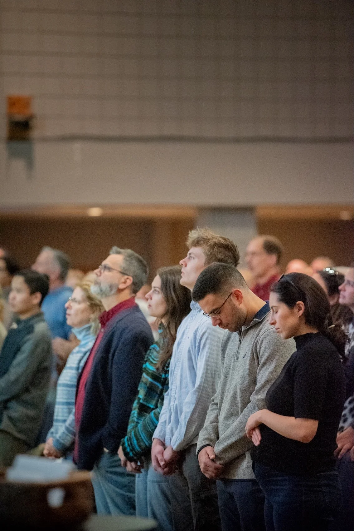 People standing in a row during a church service or prayer. Many have their heads bowed or eyes closed.