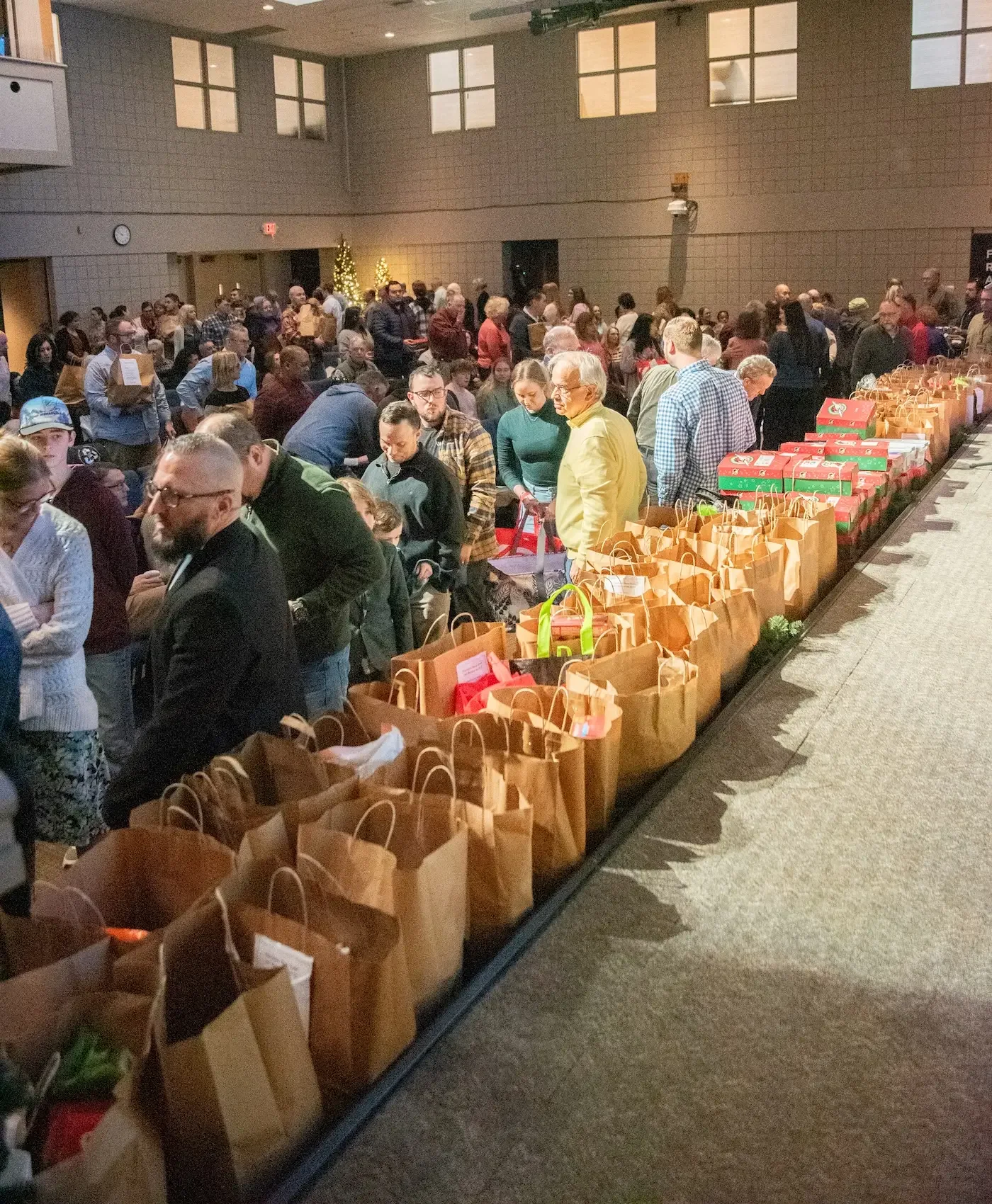 Crowd of people lining up at an event with many gift bags and wrapped presents on a long table.