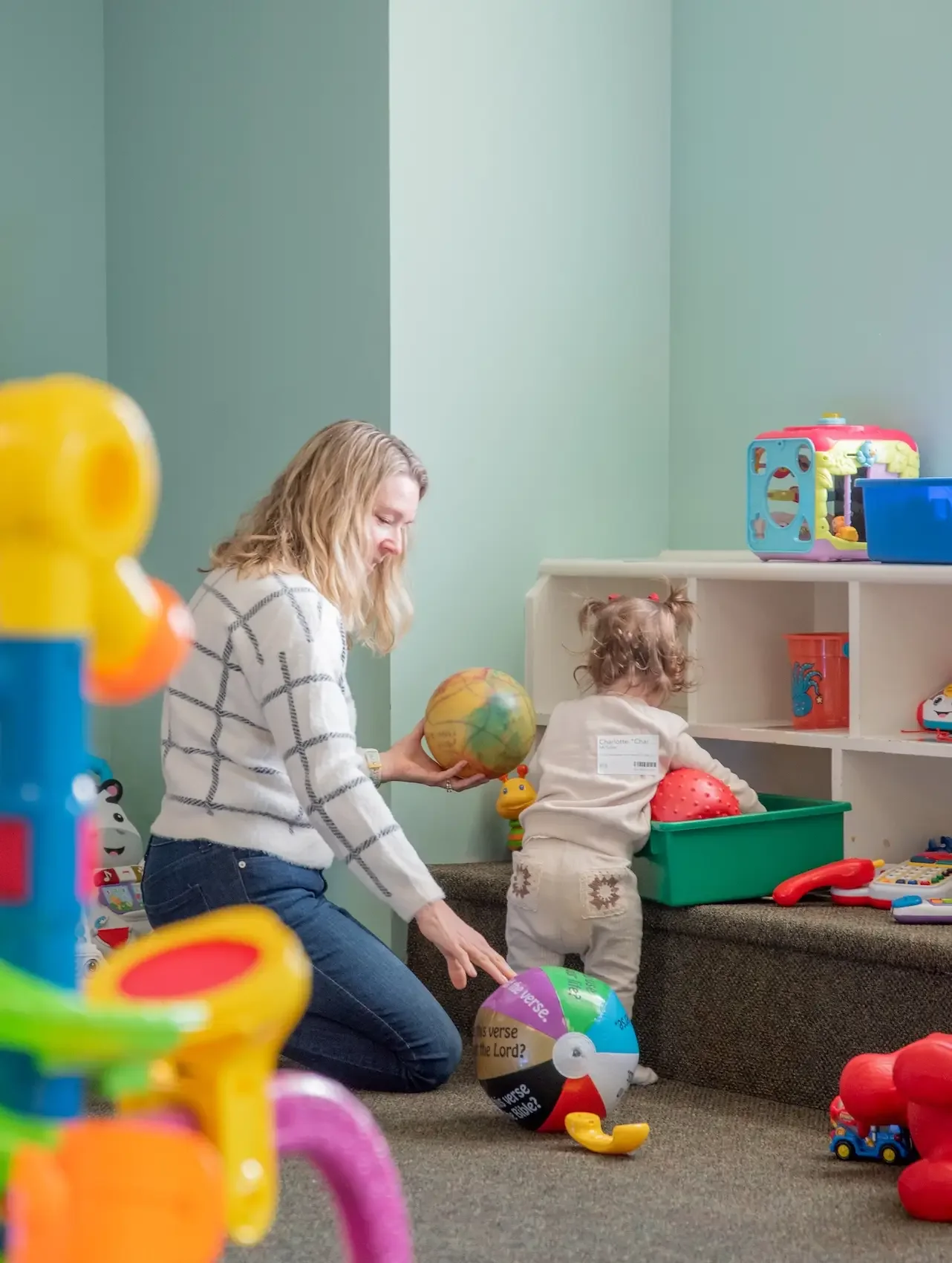 A woman and a young girl playing with colorful plastic balls in a room filled with toys.