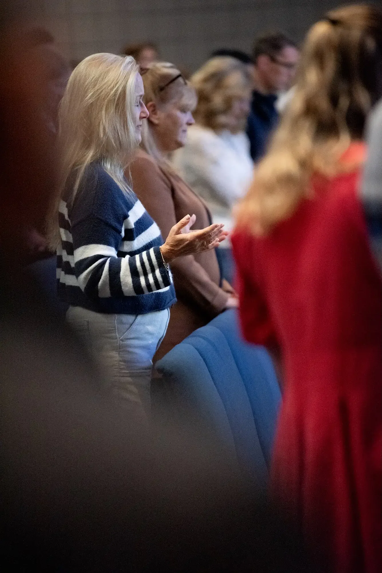 People standing with eyes closed, some with hands raised or clasped, appearing to participate in a prayer or worship session.