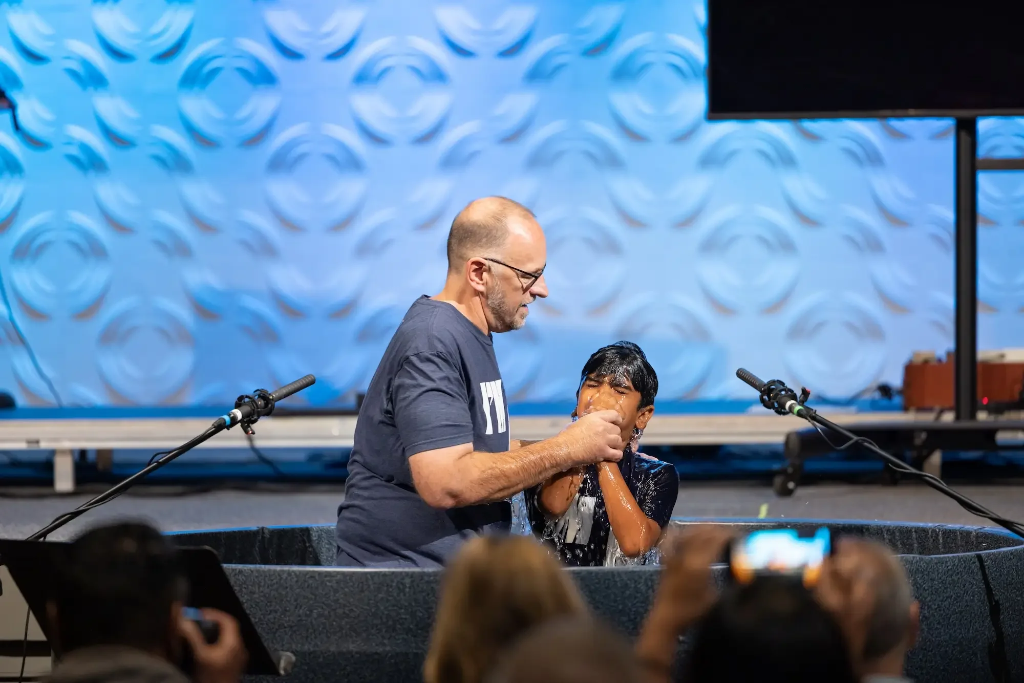 A man baptizing a young boy in a water baptism pool during a church service.