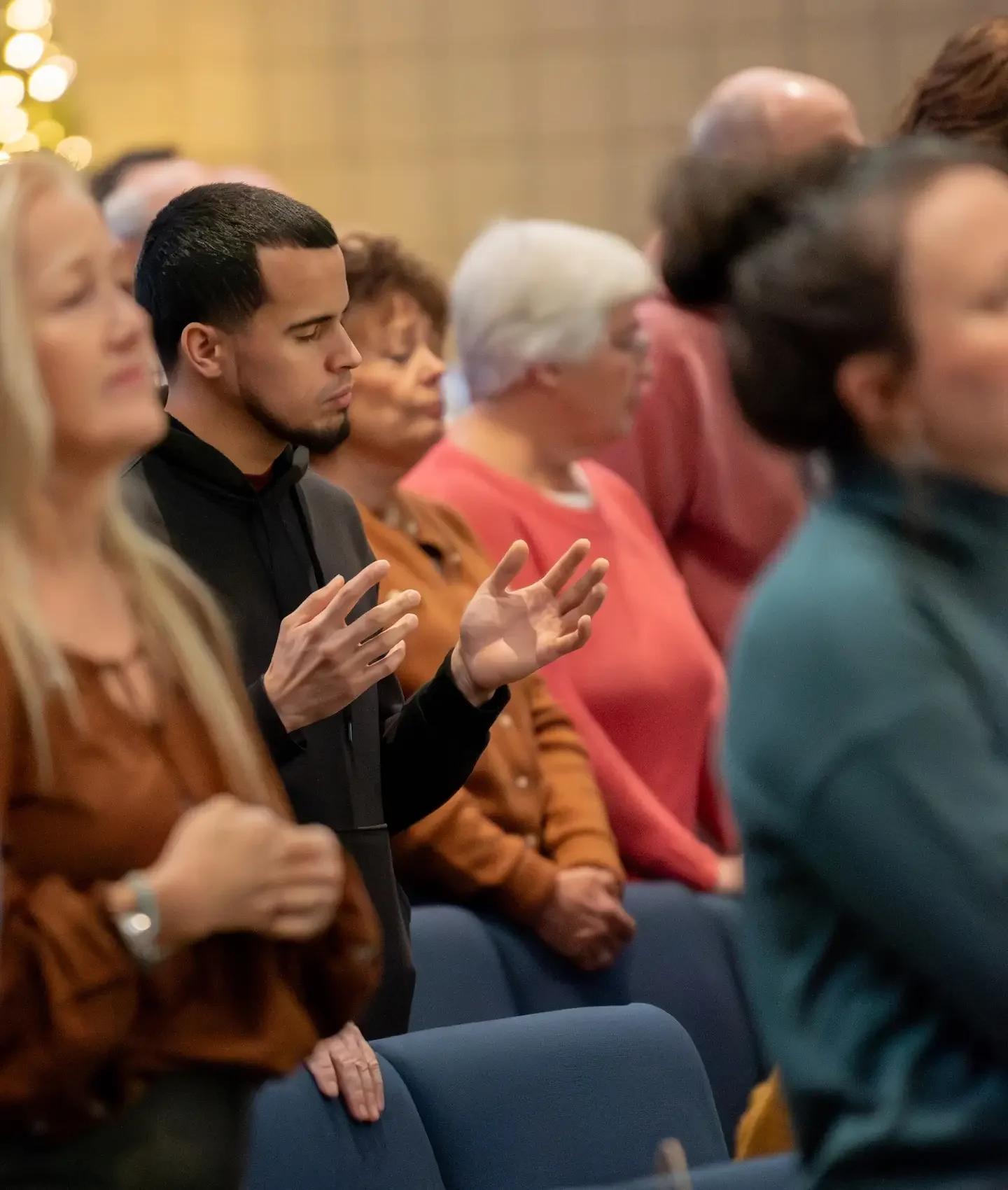 People standing with some eyes closed and hands raised, likely praying, in a religious or spiritual service.