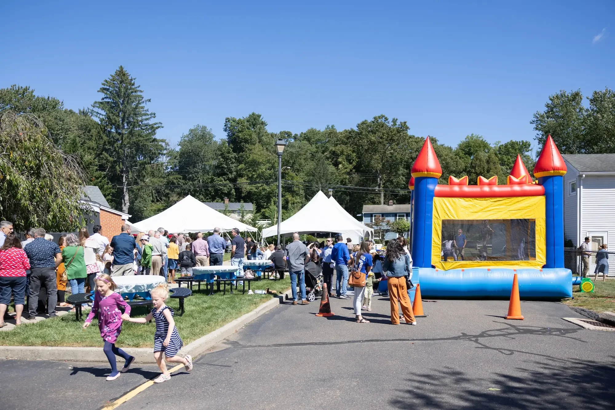 Children playing outside at a community event with food tents and a bounce house under a clear blue sky.