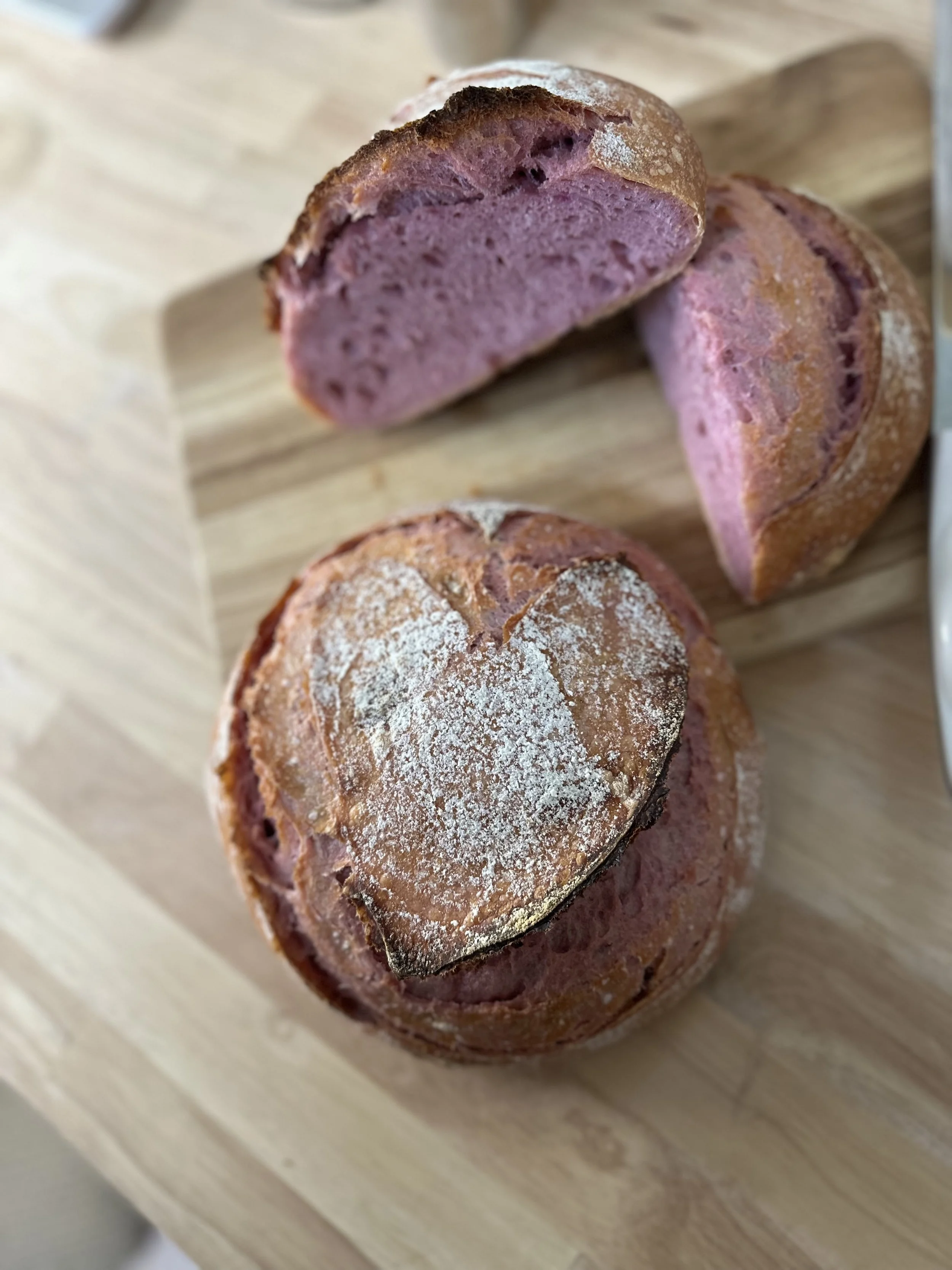 A loaf of bread with a heart-shaped crust design on top, sliced to reveal pinkish interior, placed on a wooden surface.