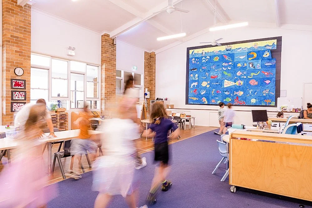 Children playing and walking inside a classroom with colorful marine life mural, desks, and chairs.