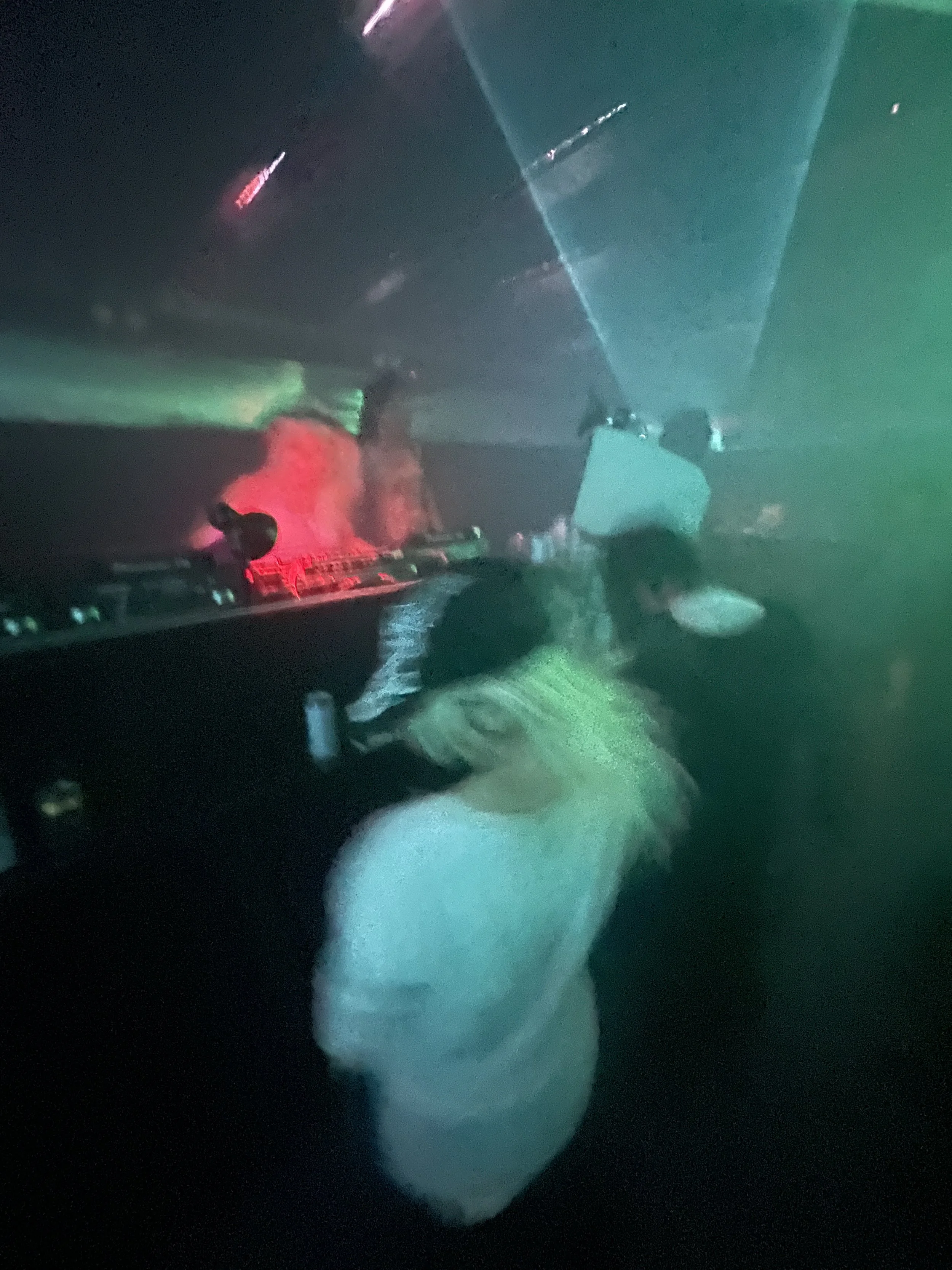 Person with long hair dancing in a dark club with colorful laser lights.